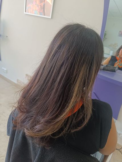 Una mujer con cabello largo está sentada frente a un espejo en un salón.