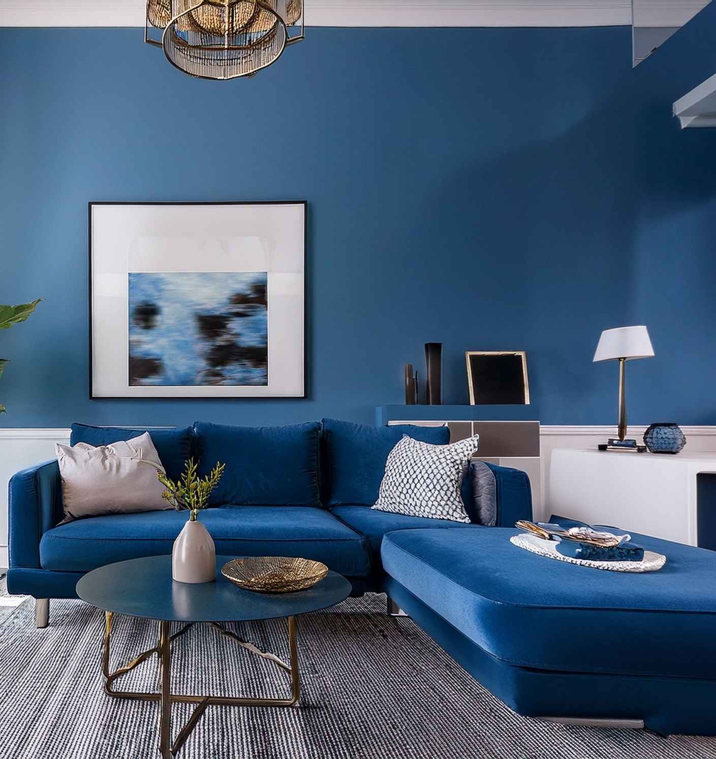 Salon bleu avec canapé d'angle, œuvres d'art et table basse.