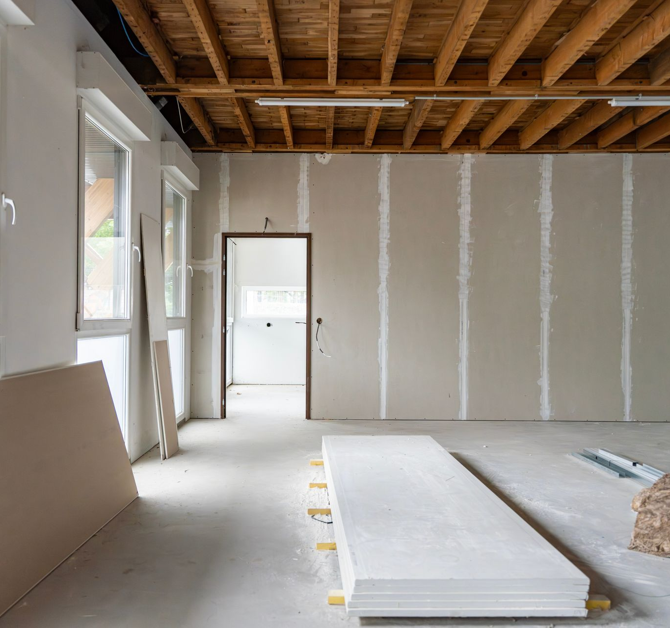 Intérieur en travaux ; murs et plafond non finis, plaques de plâtre et porte ouverte.