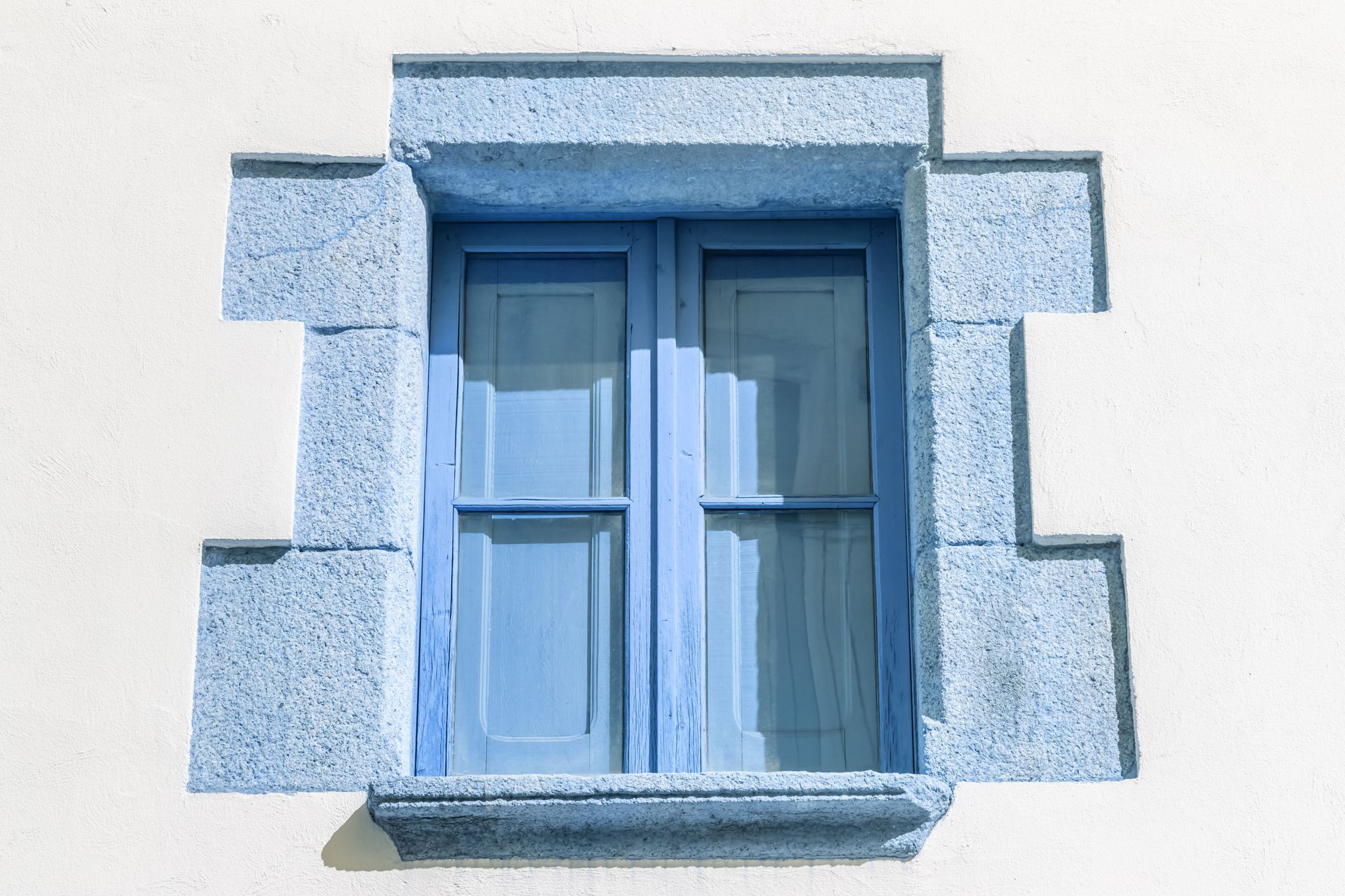 Fenêtre bleue à volets dans un cadre en pierre, encastrée dans un mur blanc.