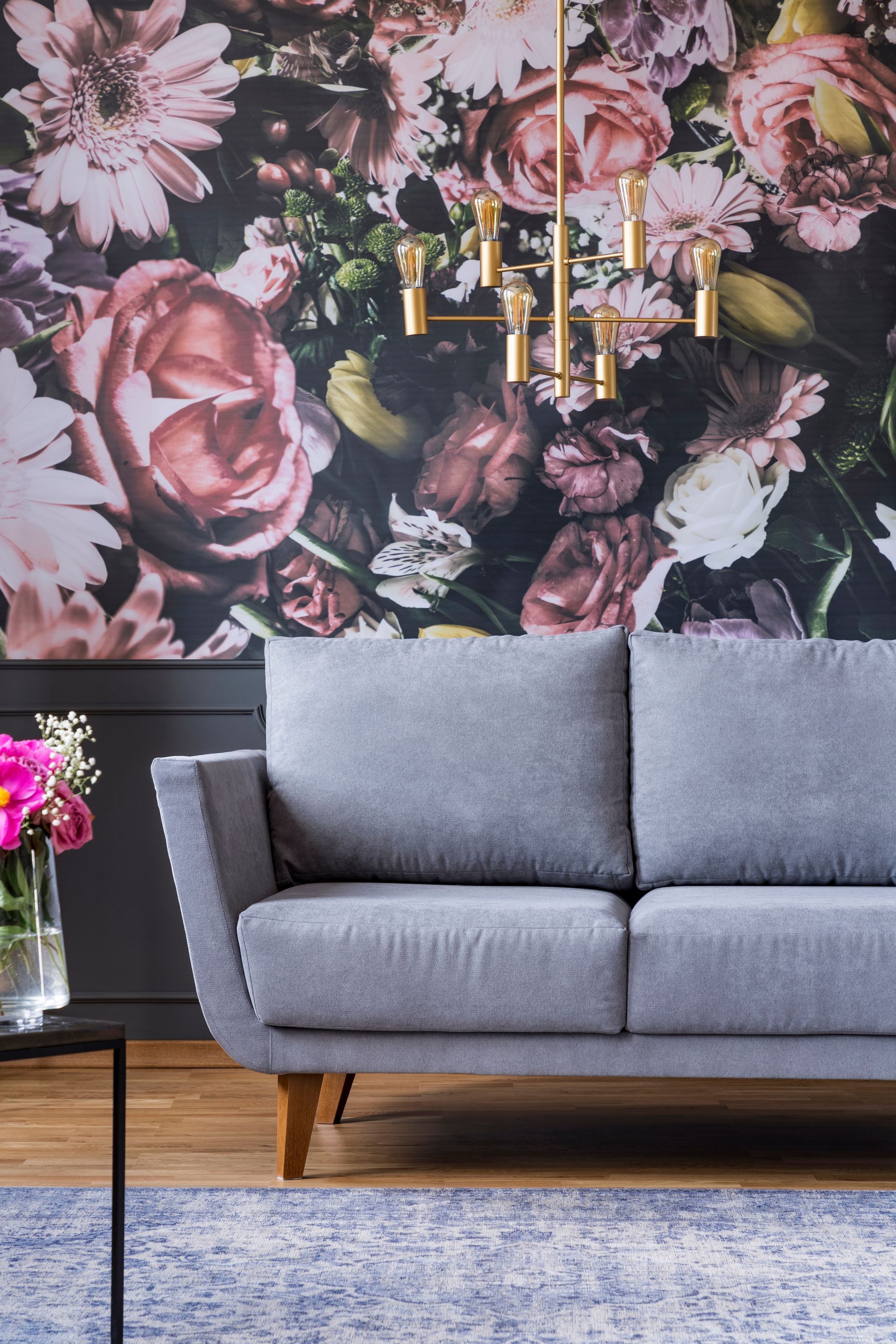 Canapé gris devant un papier peint à motifs floraux avec un lustre doré.