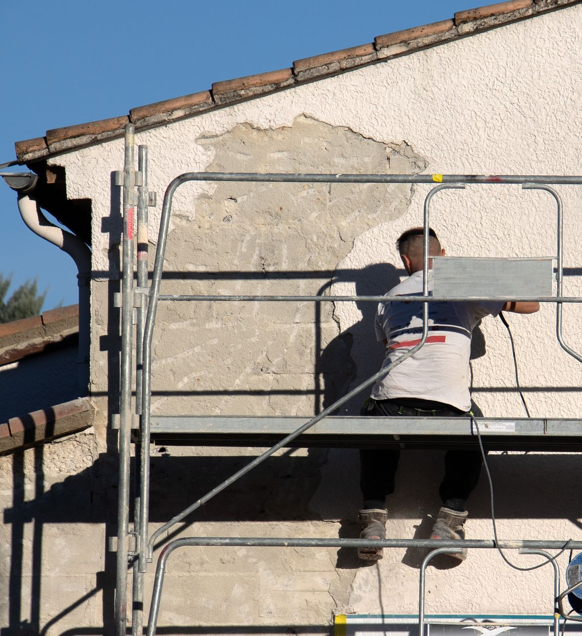 Un homme répare un mur en stuc sur un échafaudage.