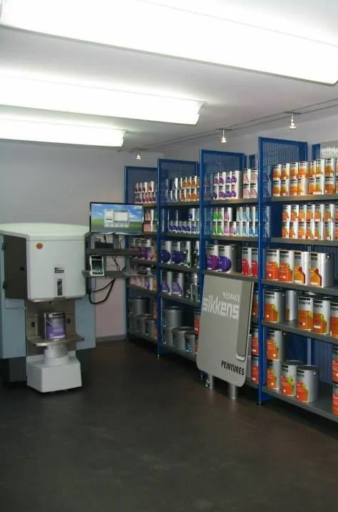 Intérieur d'un magasin de peinture avec des étagères remplies de pots de peinture et une machine à mélanger les couleurs.