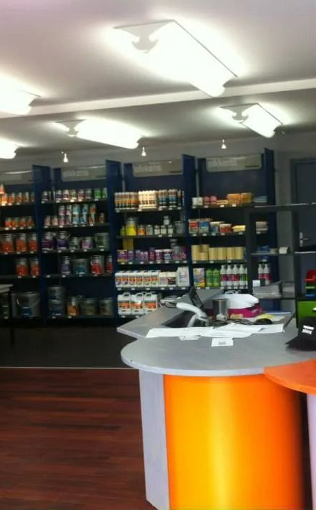 À l'intérieur d'un magasin, des étagères remplies de produits variés, un comptoir au premier plan.