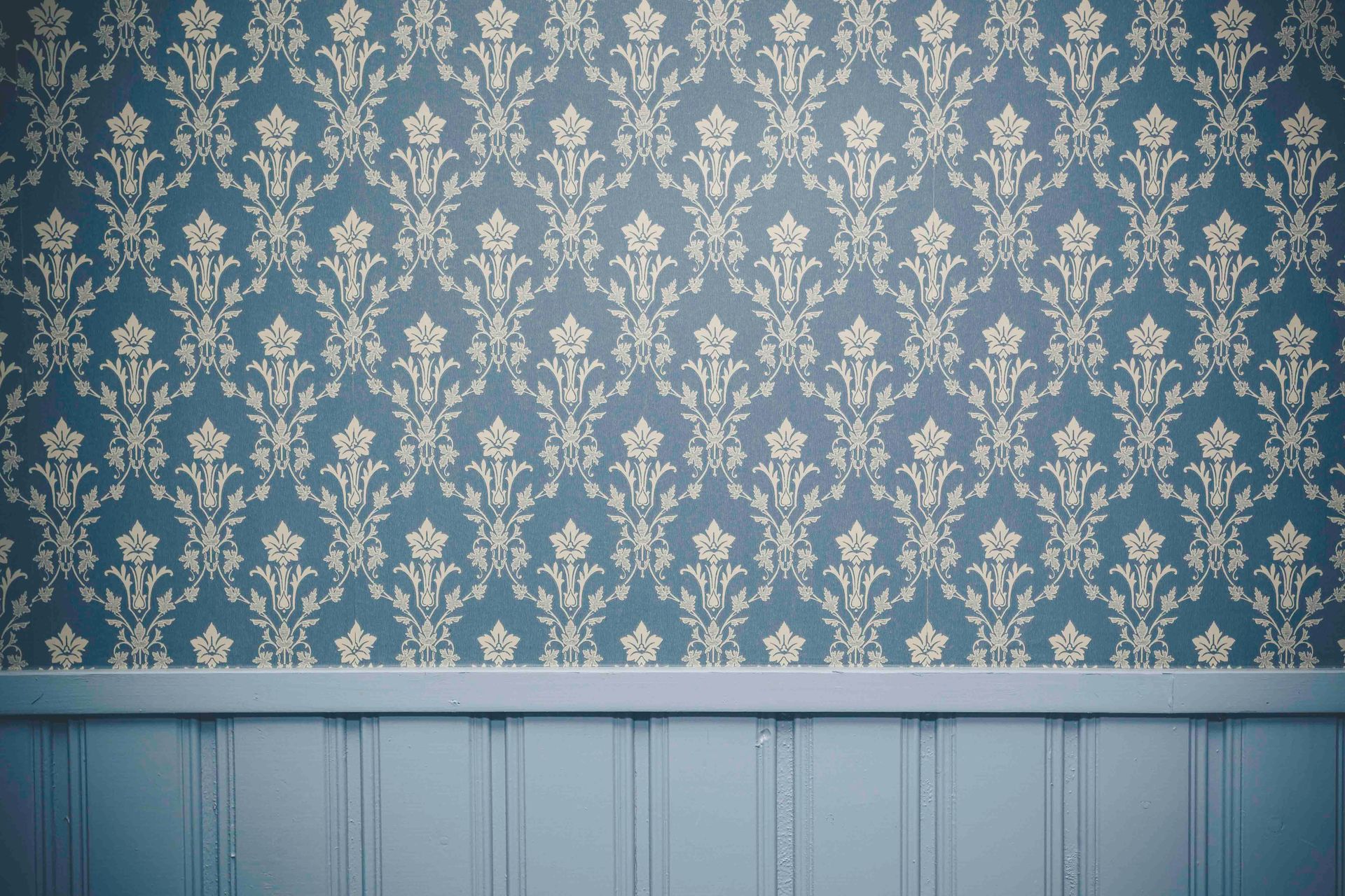 Blaue Blumentapete über hellblauer Wandvertäfelung in einem leeren Raum