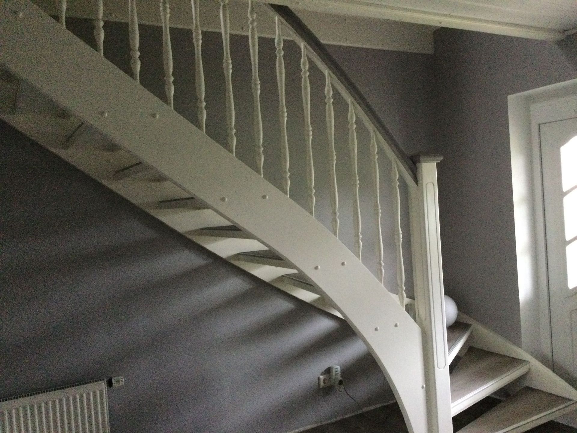 Weiße Treppe mit geschwungenem Geländer in einem grauen Innenraum in der Nähe eines Fensters.