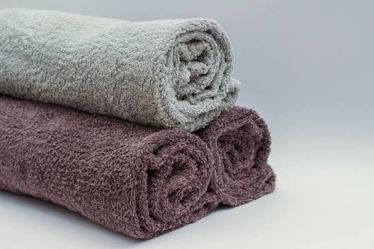 Tres toallas enrolladas, de color gris y morado, apiladas sobre una superficie blanca.