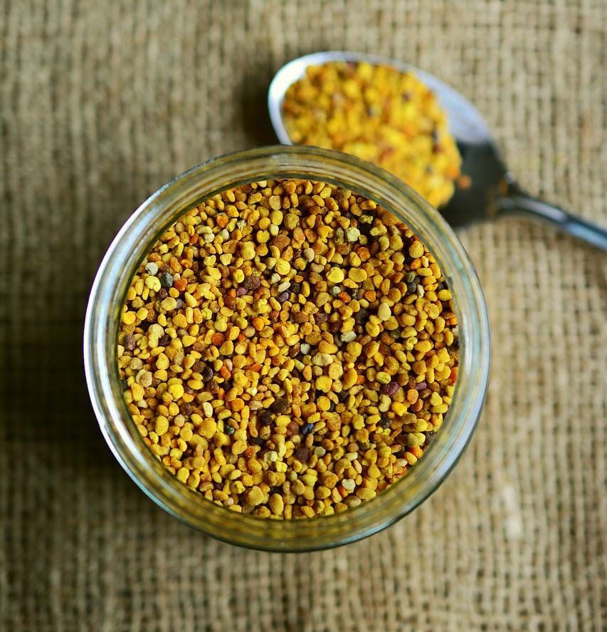 Bocal en verre contenant du pollen d'abeille jaune et brun, avec une cuillère posée sur un morceau de toile de jute.