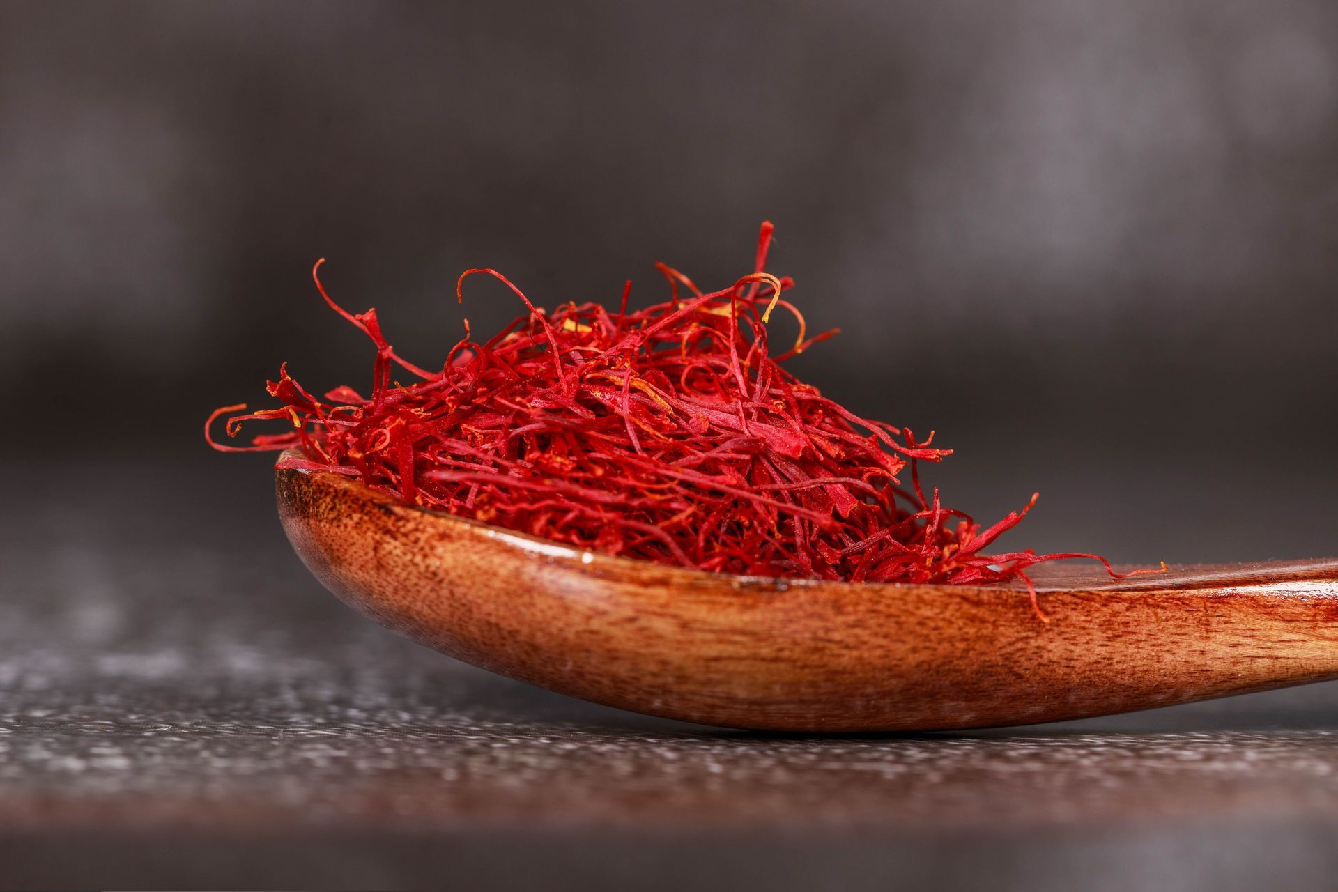 Cuillère en bois tenant un monticule de filaments de safran rouge vif sur une surface sombre