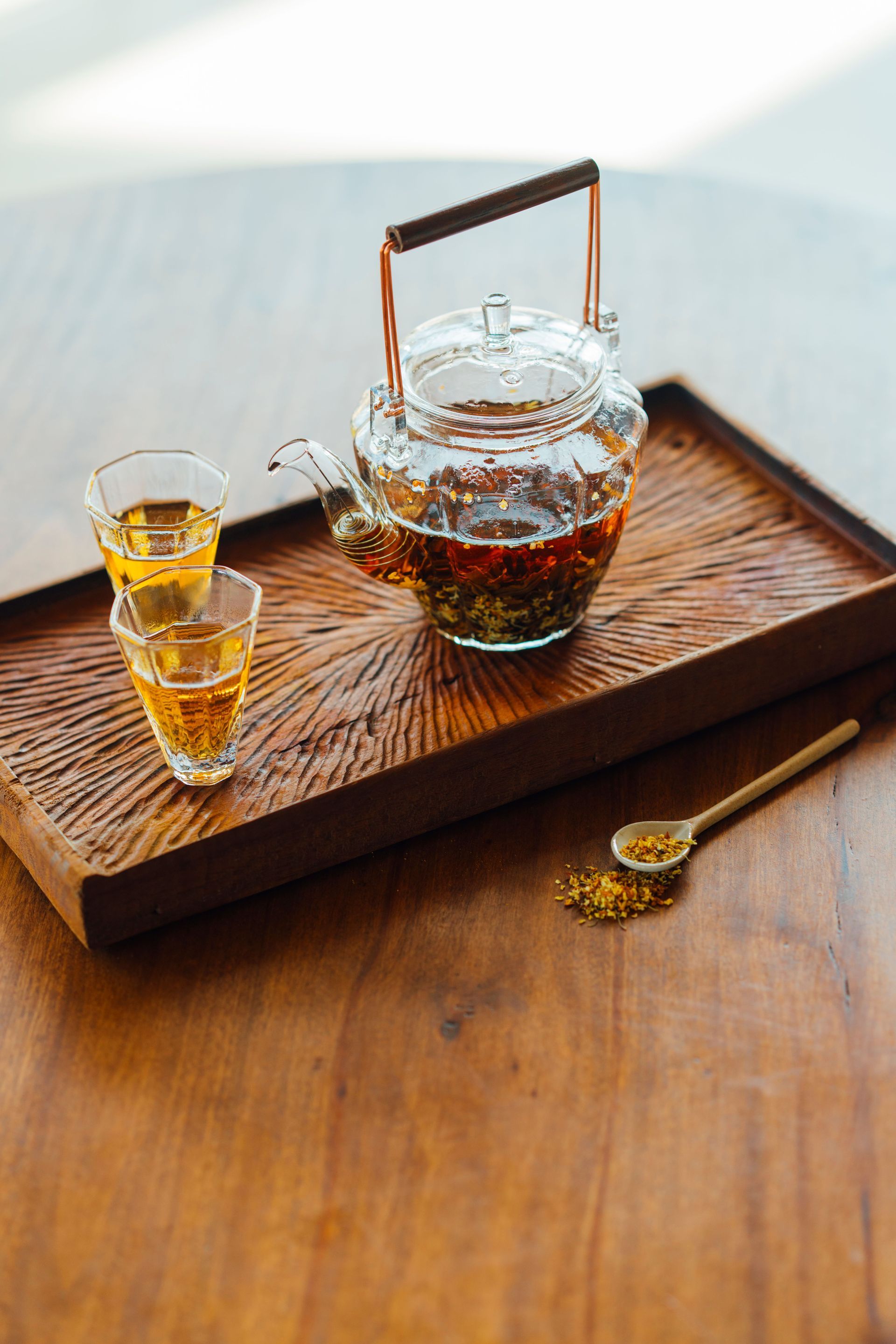 Théière en verre avec du thé et deux petites tasses sur un plateau en bois à côté d'une cuillère