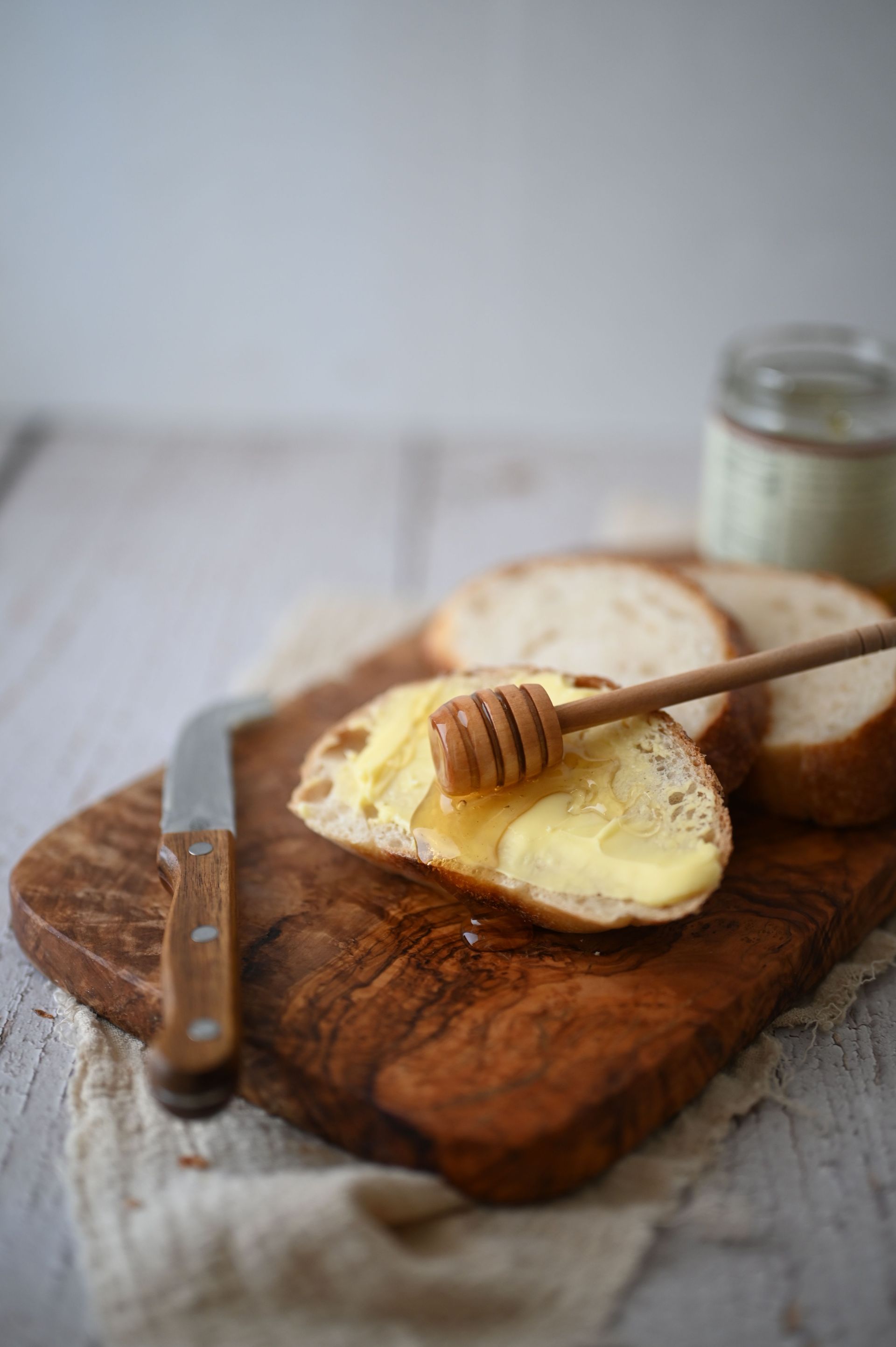Du pain beurré avec du miel sur une planche à découper en bois, avec un couteau et un pot à proximité.