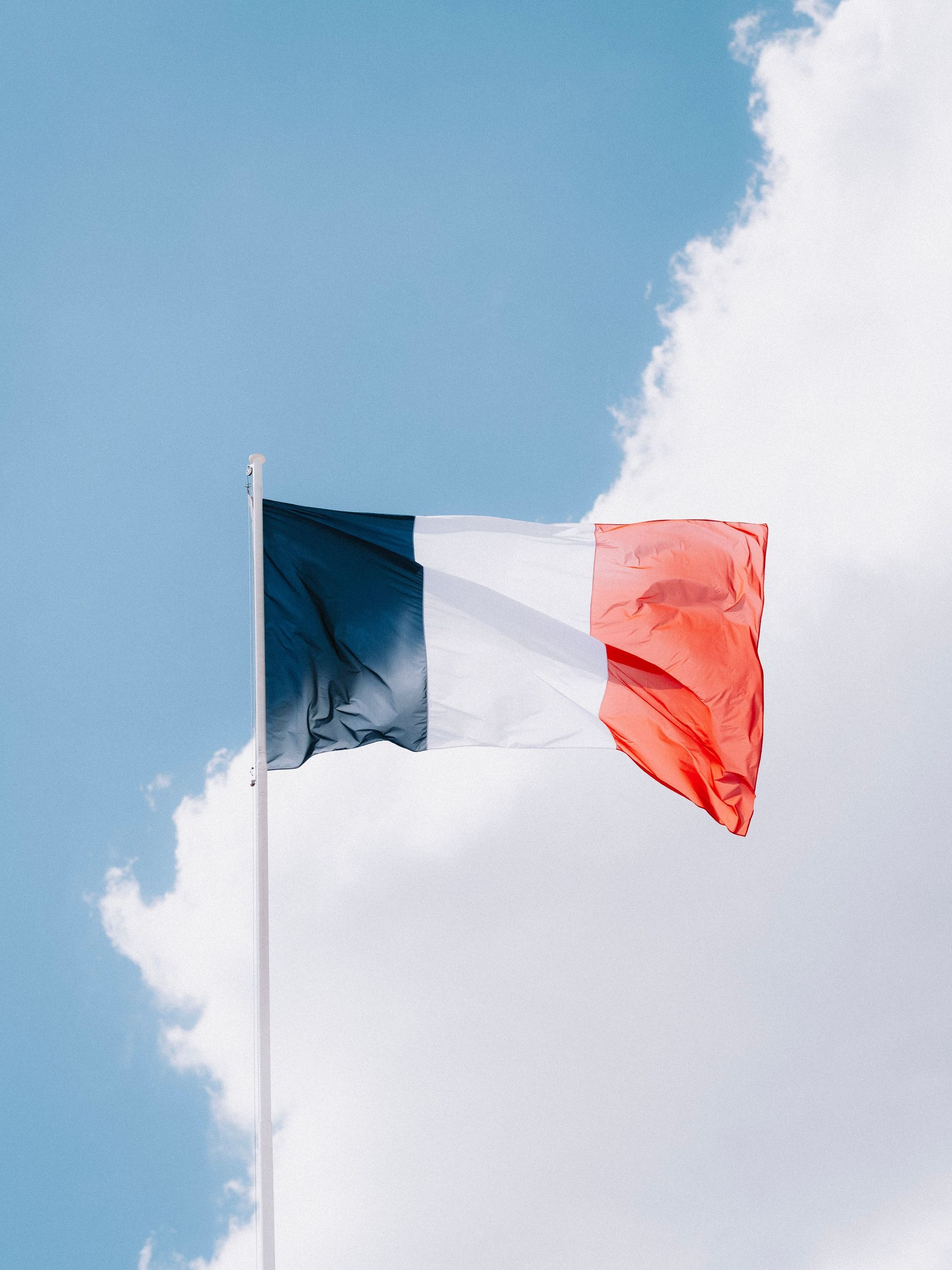 Drapeau français flottant sur un ciel bleu parsemé de nuages