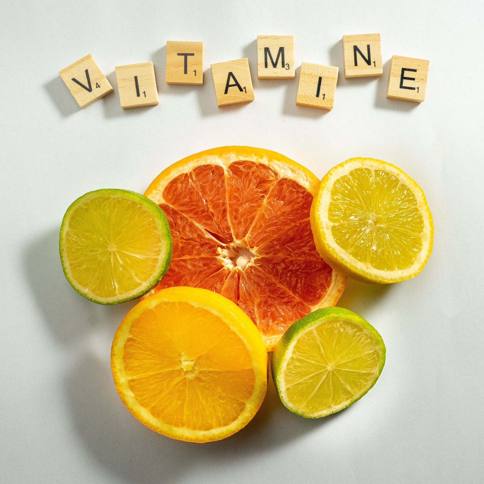 Le mot « vitamine » est écrit en lettres de bois au-dessus de tranches d'agrumes sur fond blanc.