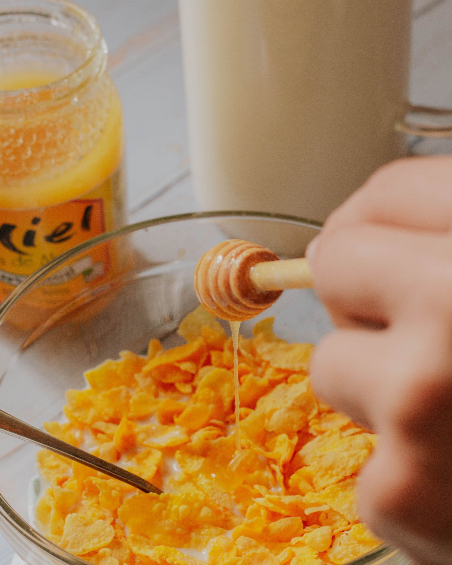 Du miel versé sur des céréales dans un bol, à côté d'un pot de miel et d'un verre de lait.