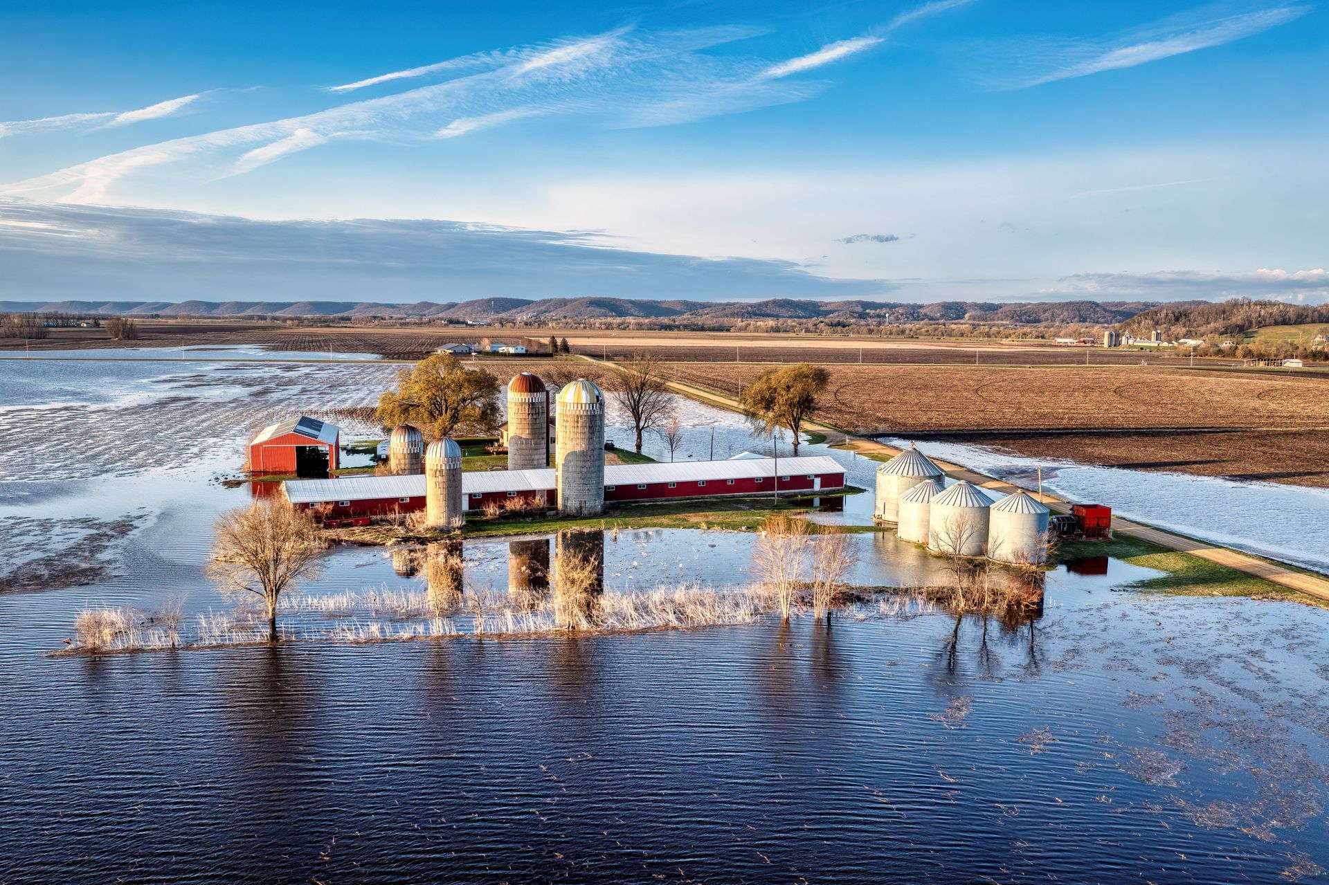 Champ inondé avec des structures industrielles blanches et un petit bâtiment rouge sous un ciel bleu