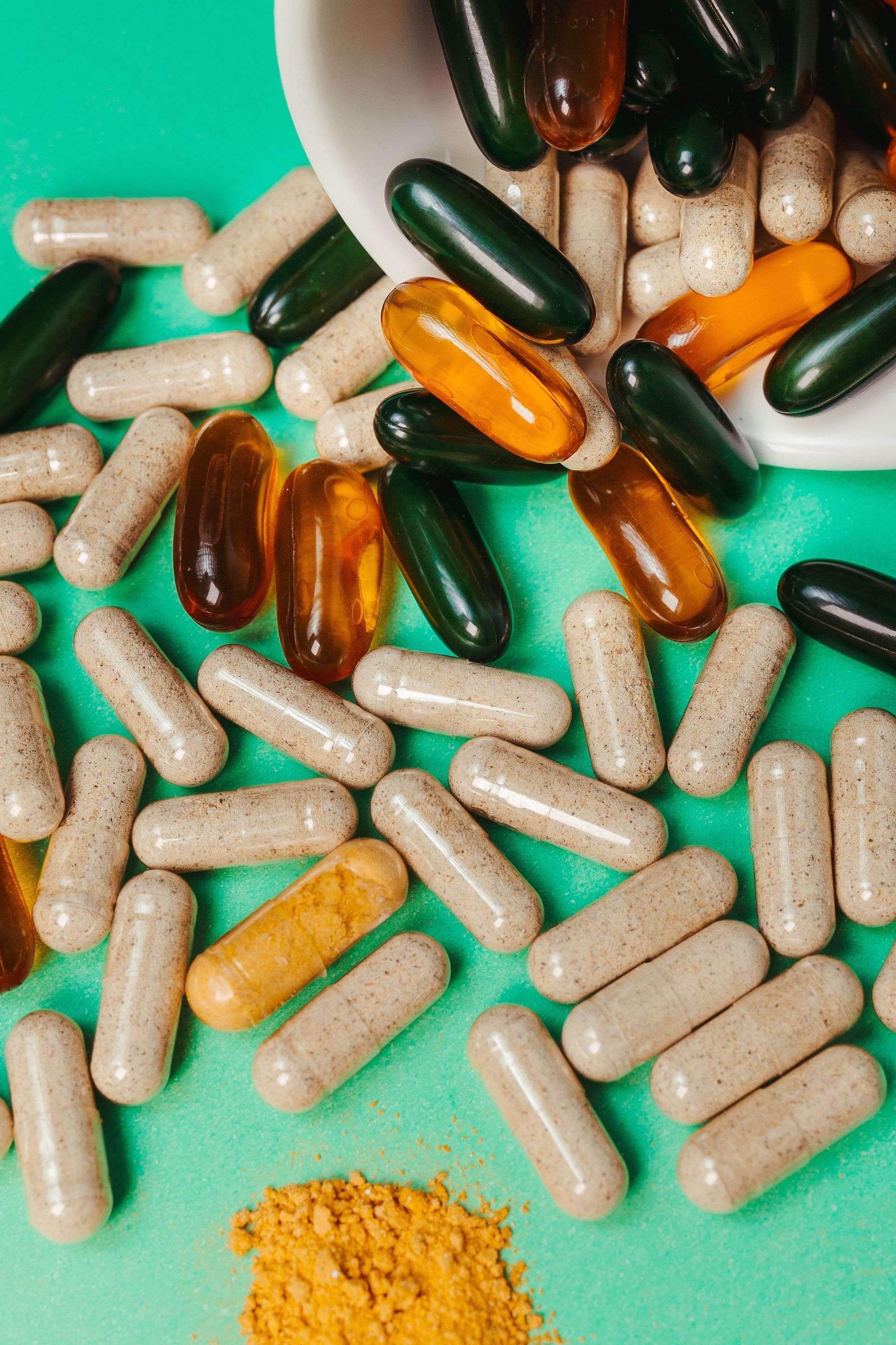 Capsules beiges, vertes, ambrées et blanches éparpillées avec un petit tas de poudre jaune sur un fond menthe
