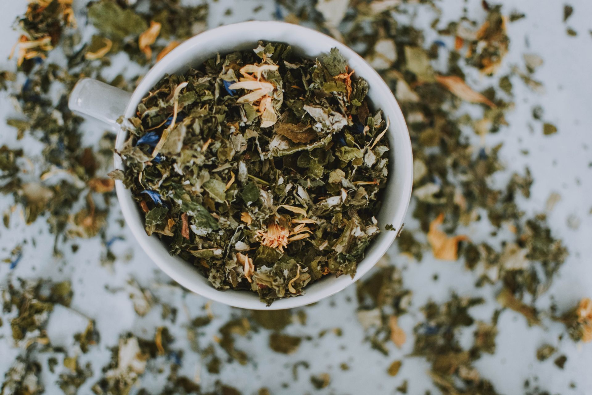 Tasse blanche remplie de feuilles de thé séchées en vrac sur une surface blanche mouchetée