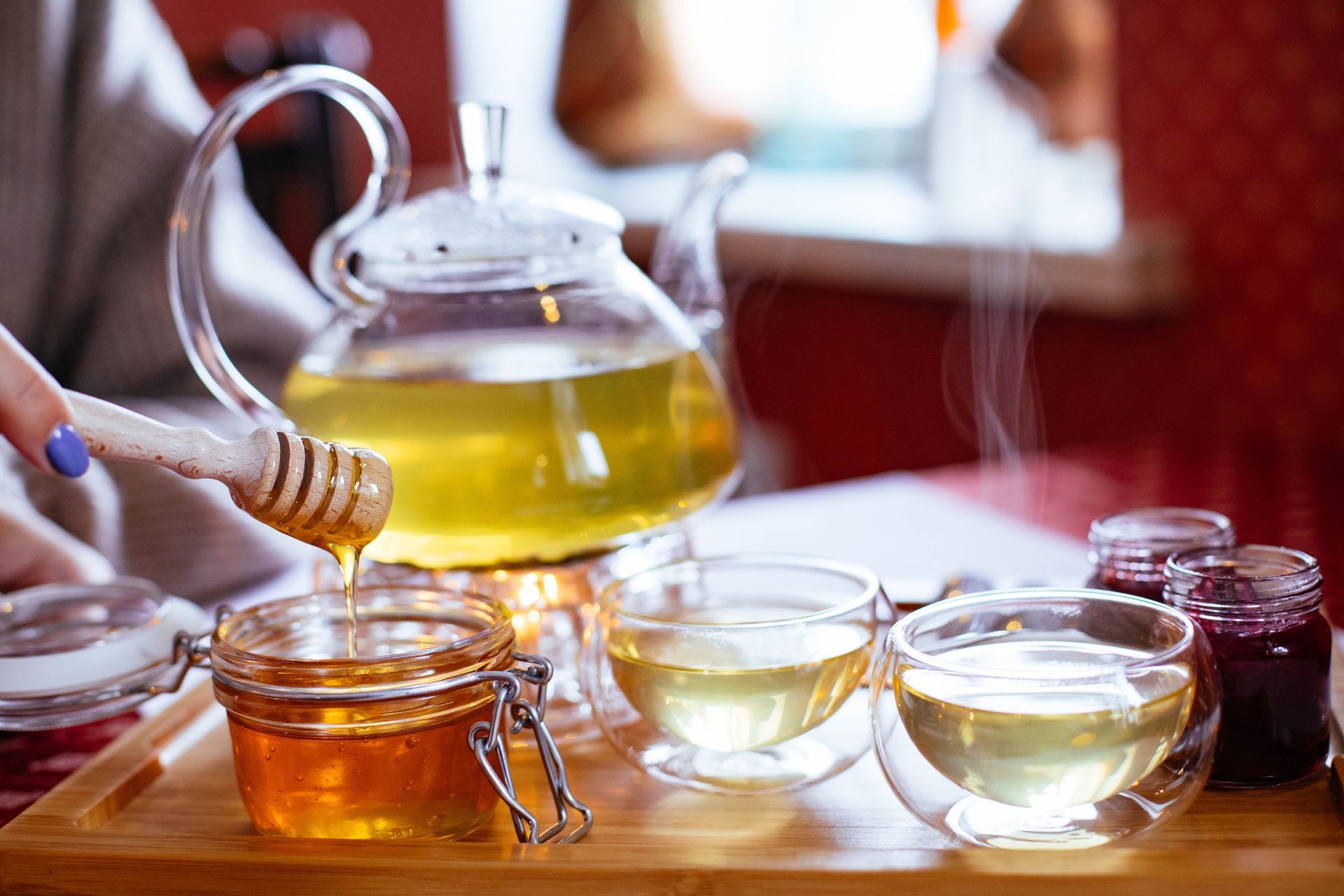 On verse du thé dans un bocal en verre à côté d'une théière et de tasses posées sur une table en bois.