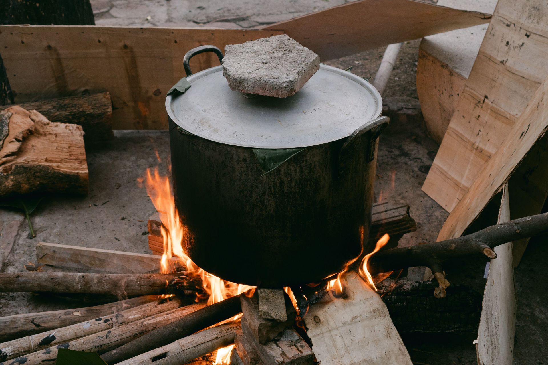 Grande marmite noire avec couvercle, en train de bouillir sur un feu de bois dans un cadre rustique extérieur