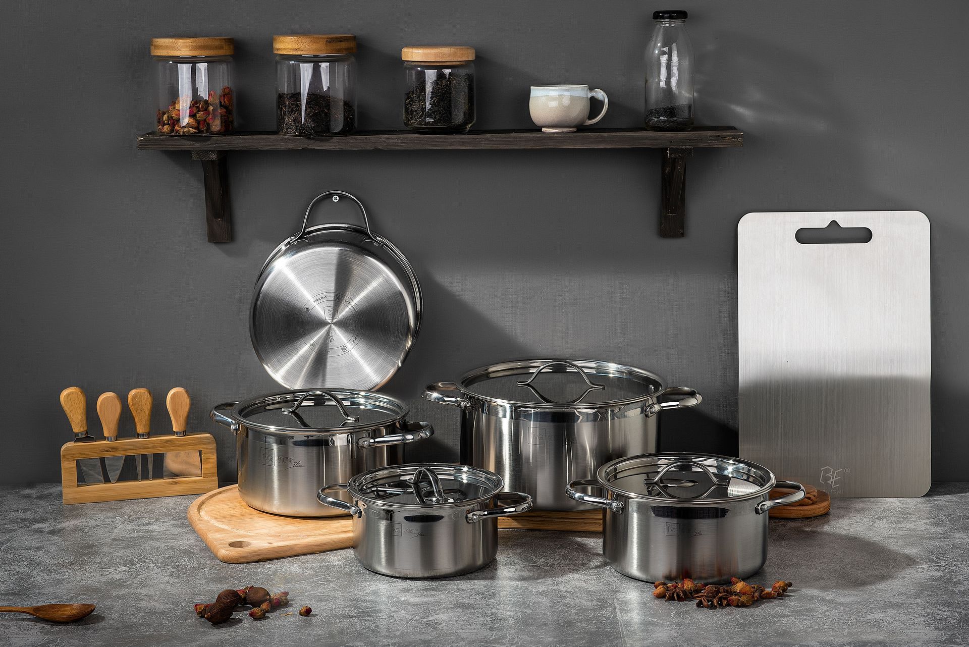 Ensemble de casseroles en acier inoxydable sur un plan de travail gris avec étagères, bocaux, tasses et ustensiles dans une cuisine moderne.