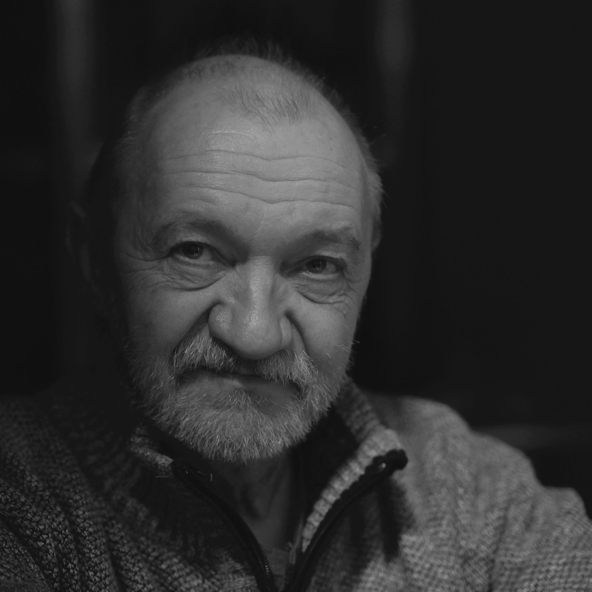 Portrait en gros plan, en noir et blanc, d'un homme barbu portant un pull, regardant l'objectif avec une expression calme.