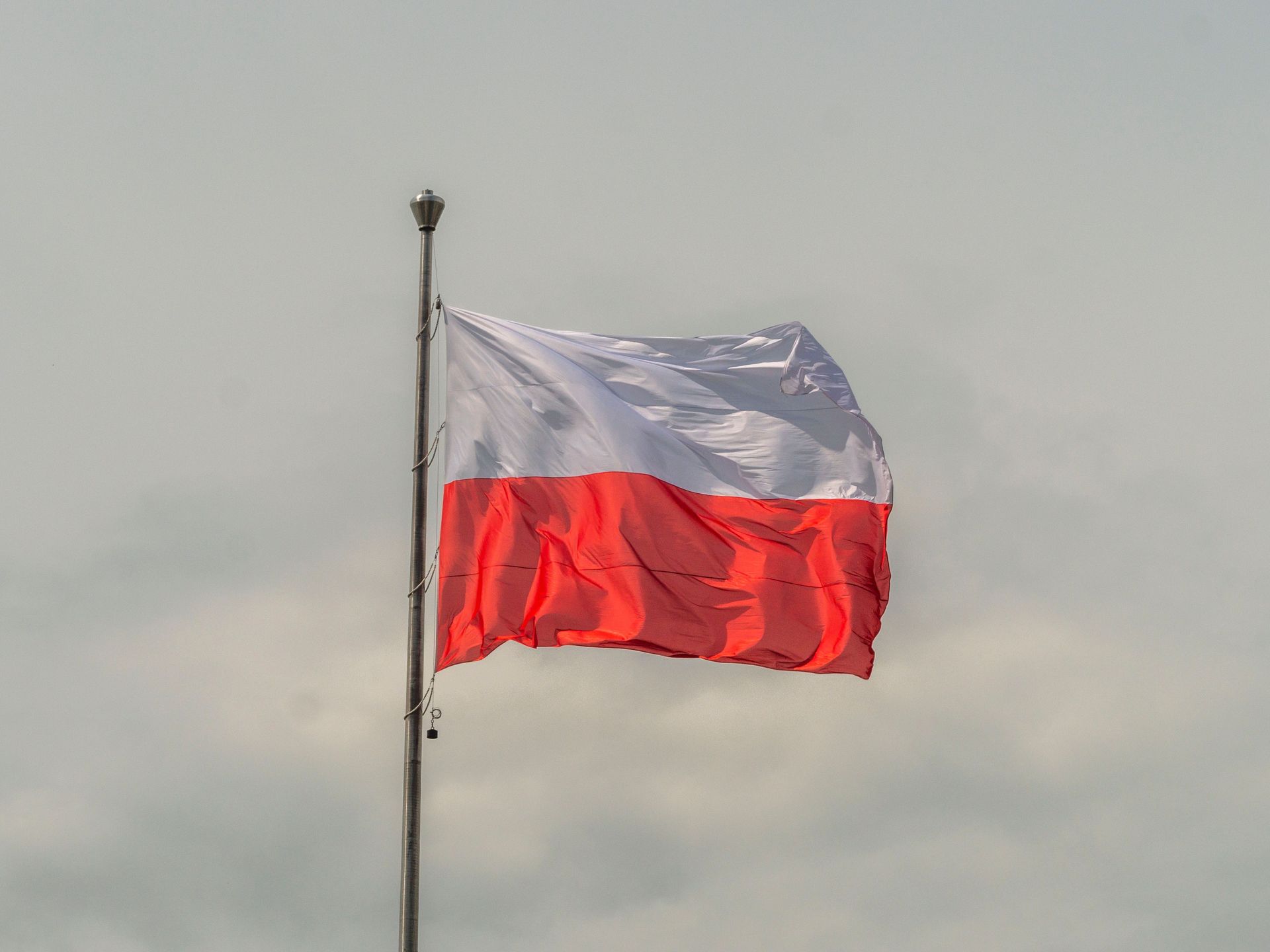 Un drapeau rouge et blanc flotte au sommet d'un grand mât sur un ciel nuageux.