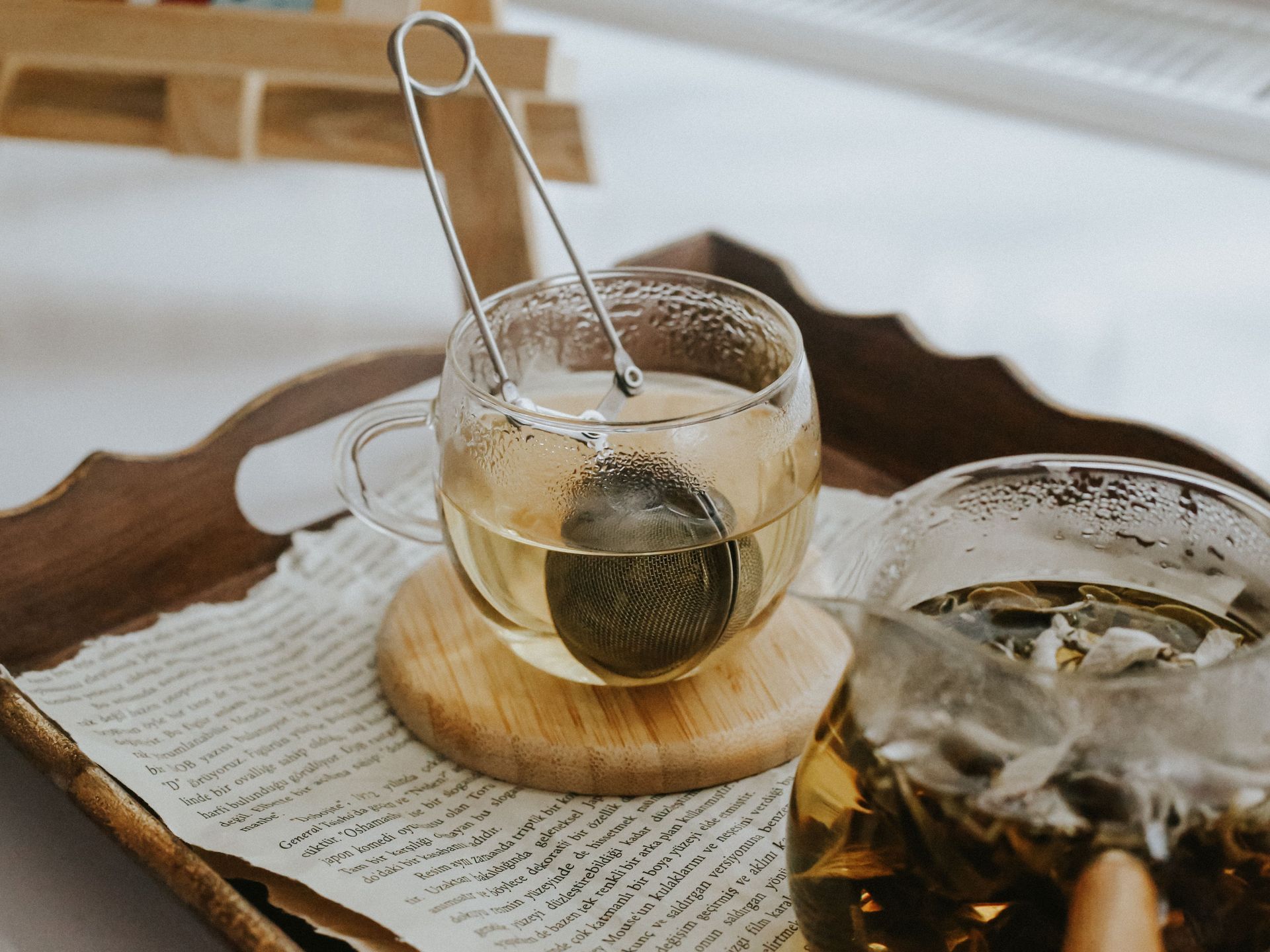 Une tasse de thé en verre posée sur un plateau en bois, avec un sachet de thé et un deuxième verre en arrière-plan.