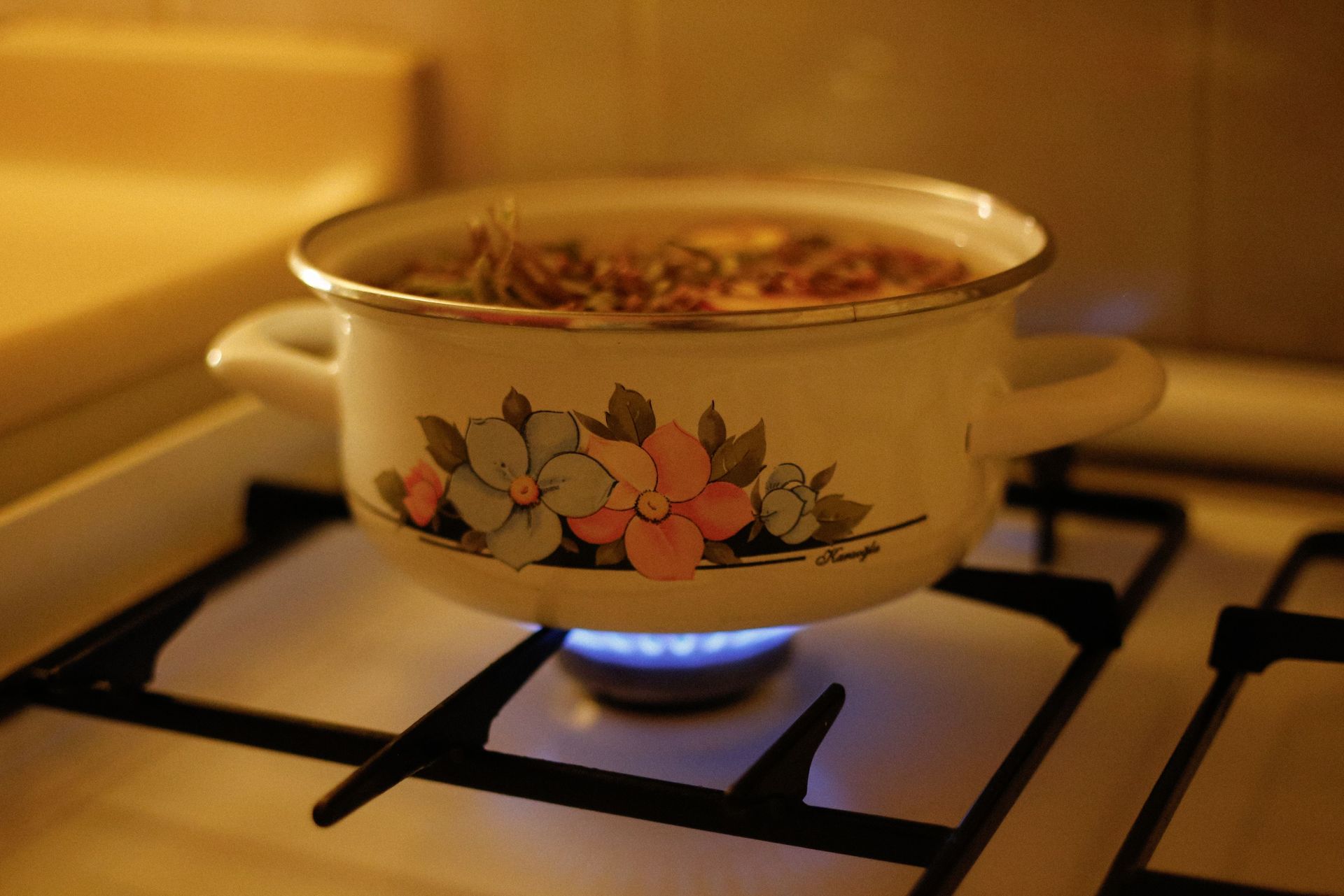 Une casserole en émail à motifs floraux mijote sur un réchaud à gaz, au-dessus d'une flamme bleue.