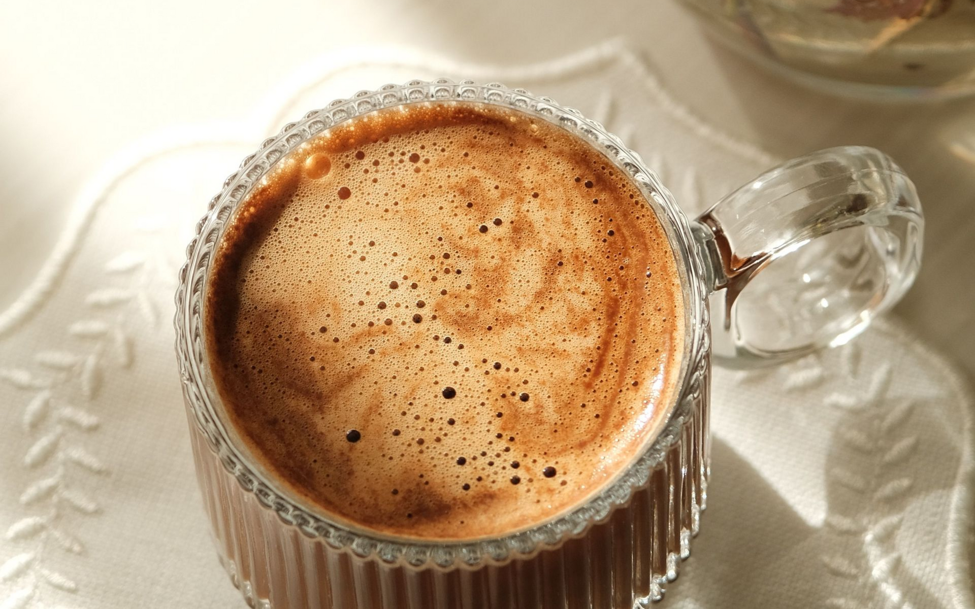 Vue de dessus d'un cappuccino mousseux dans une tasse en verre transparent posée sur une soucoupe blanche.