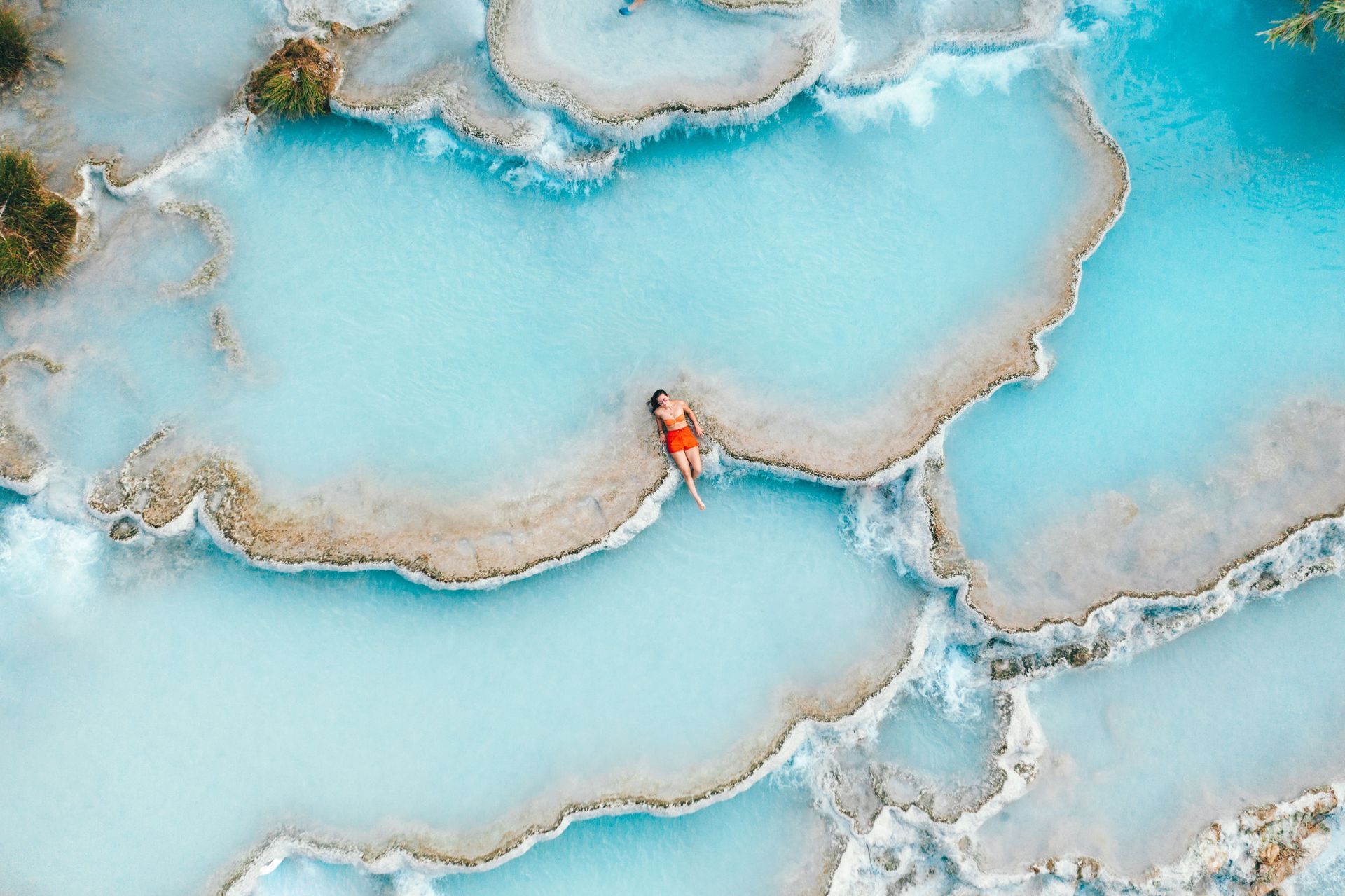 Femme assise sur le bord d'un bassin naturel vu du ciel.