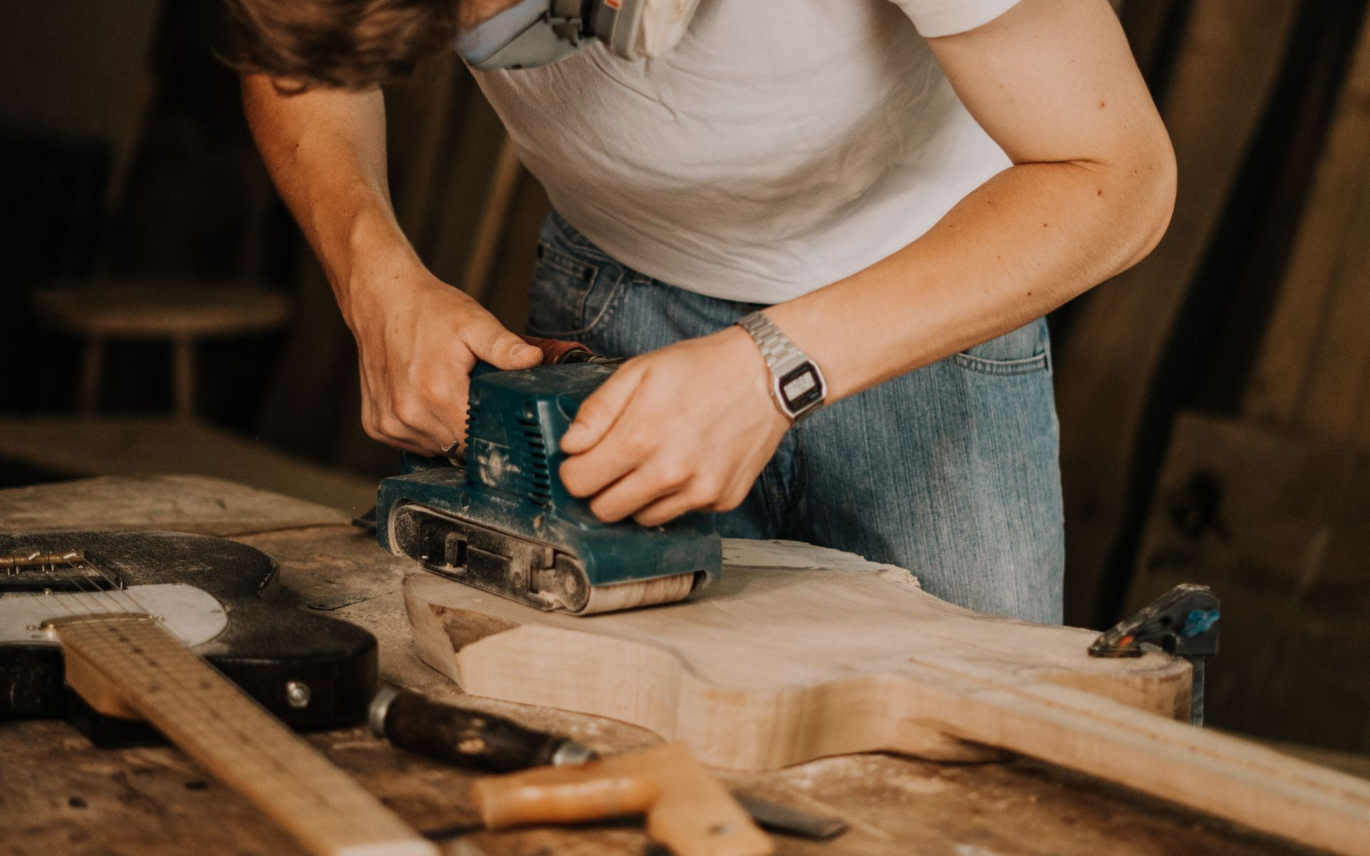 Une personne utilise une ponceuse électrique verte sur une planche de bois dans un atelier.