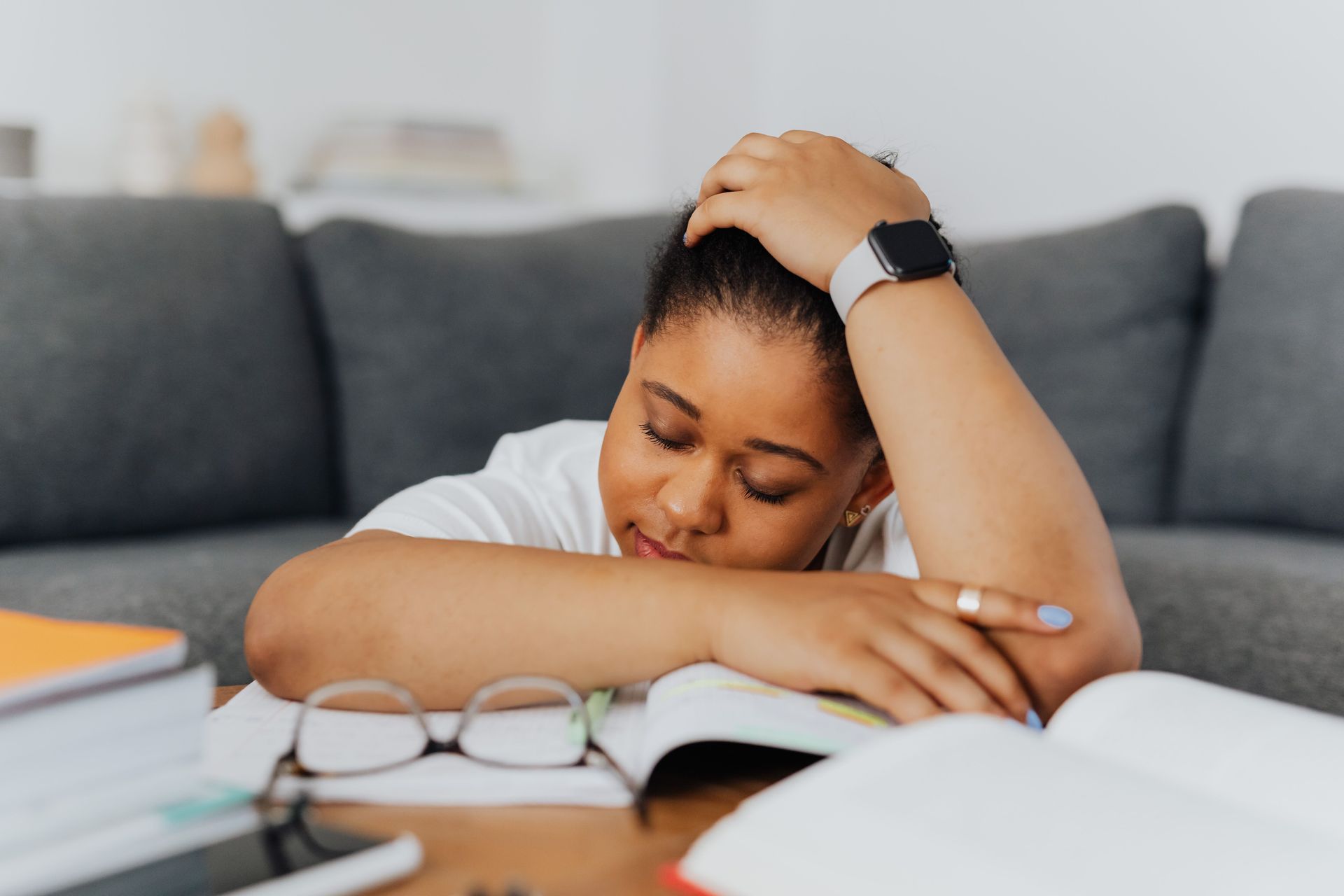 Femme aux cheveux bouclés, vêtue d’un t-shirt blanc, assise et penchée en avant, les mains posées sur le bas-ventre, illustrant des douleurs abdominales ou des crampes menstruelles