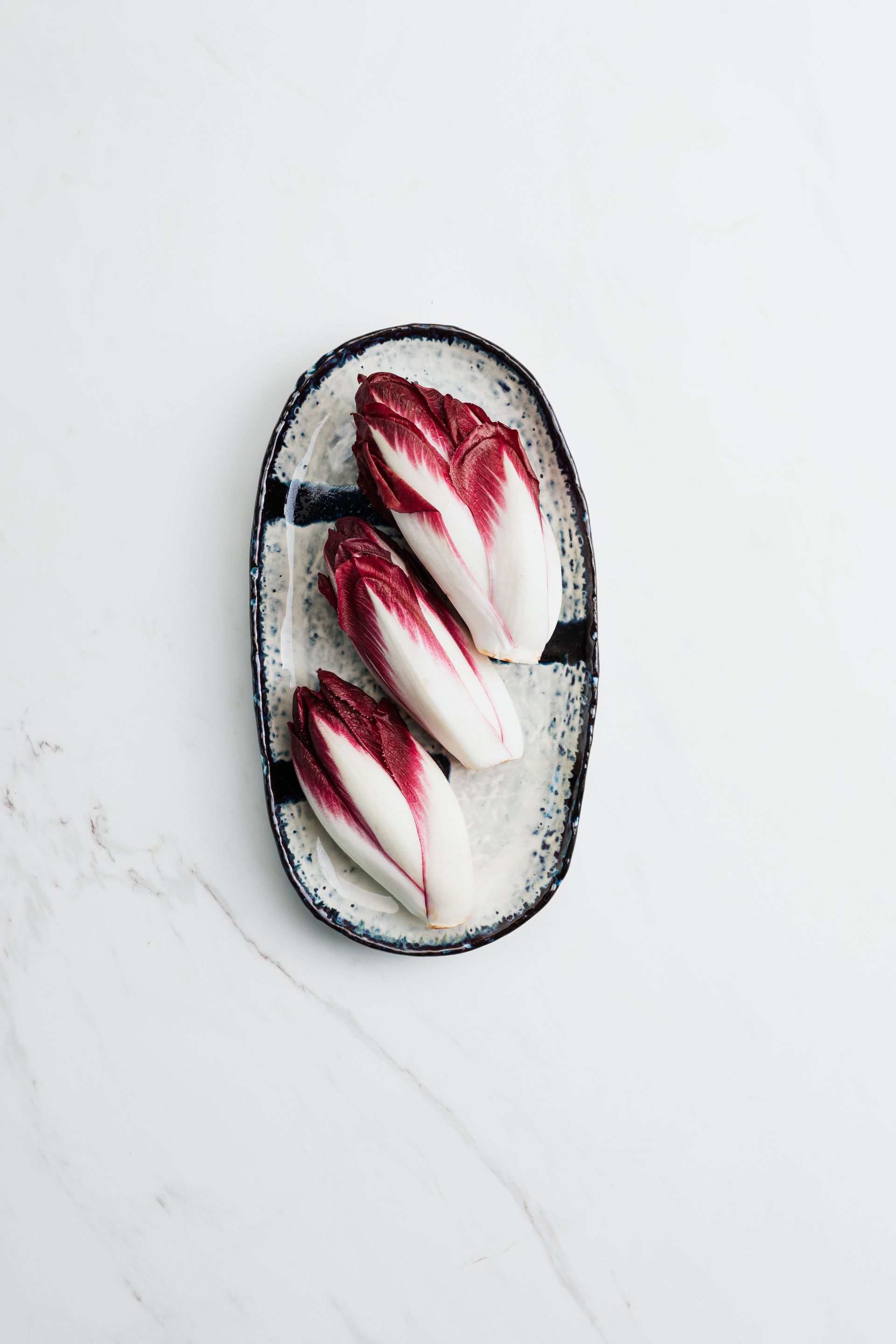 Assiette ovale avec une endive rouge sur une surface en marbre blanc