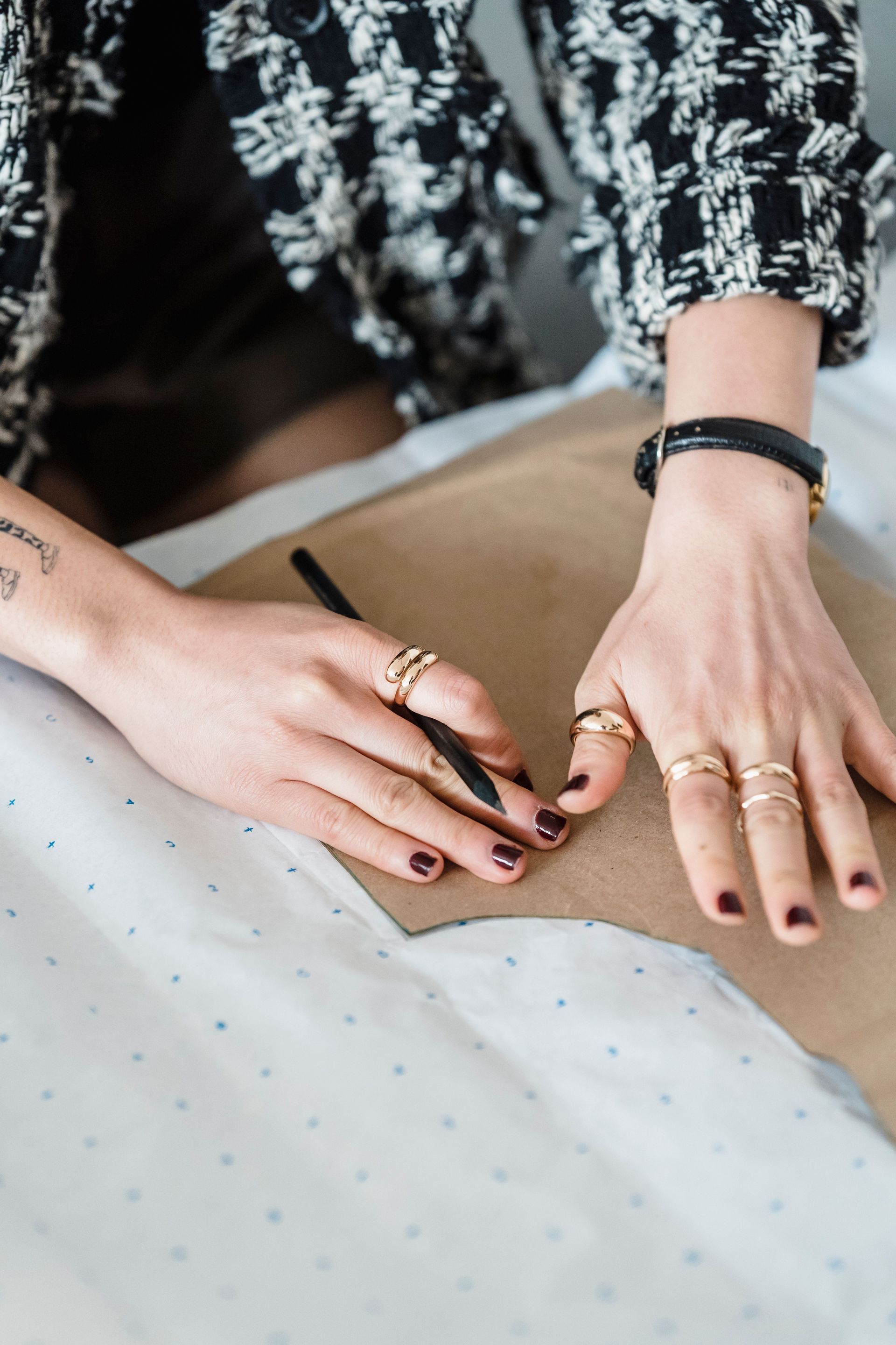 Des mains écrivent sur du papier à une table, on aperçoit des bagues et un bracelet noir.