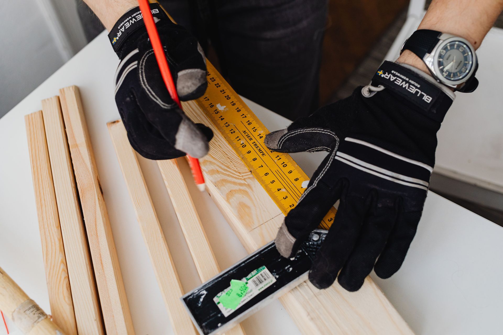 Personne utilisant un crayon et des outils de mesure pour marquer des planches de bois sur un établi