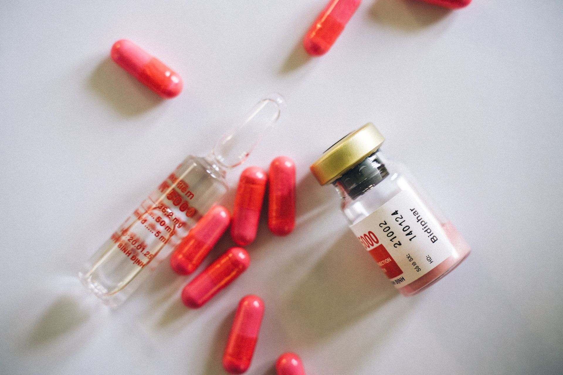 Des capsules rouges et des flacons de médicaments éparpillés sur une surface blanche.