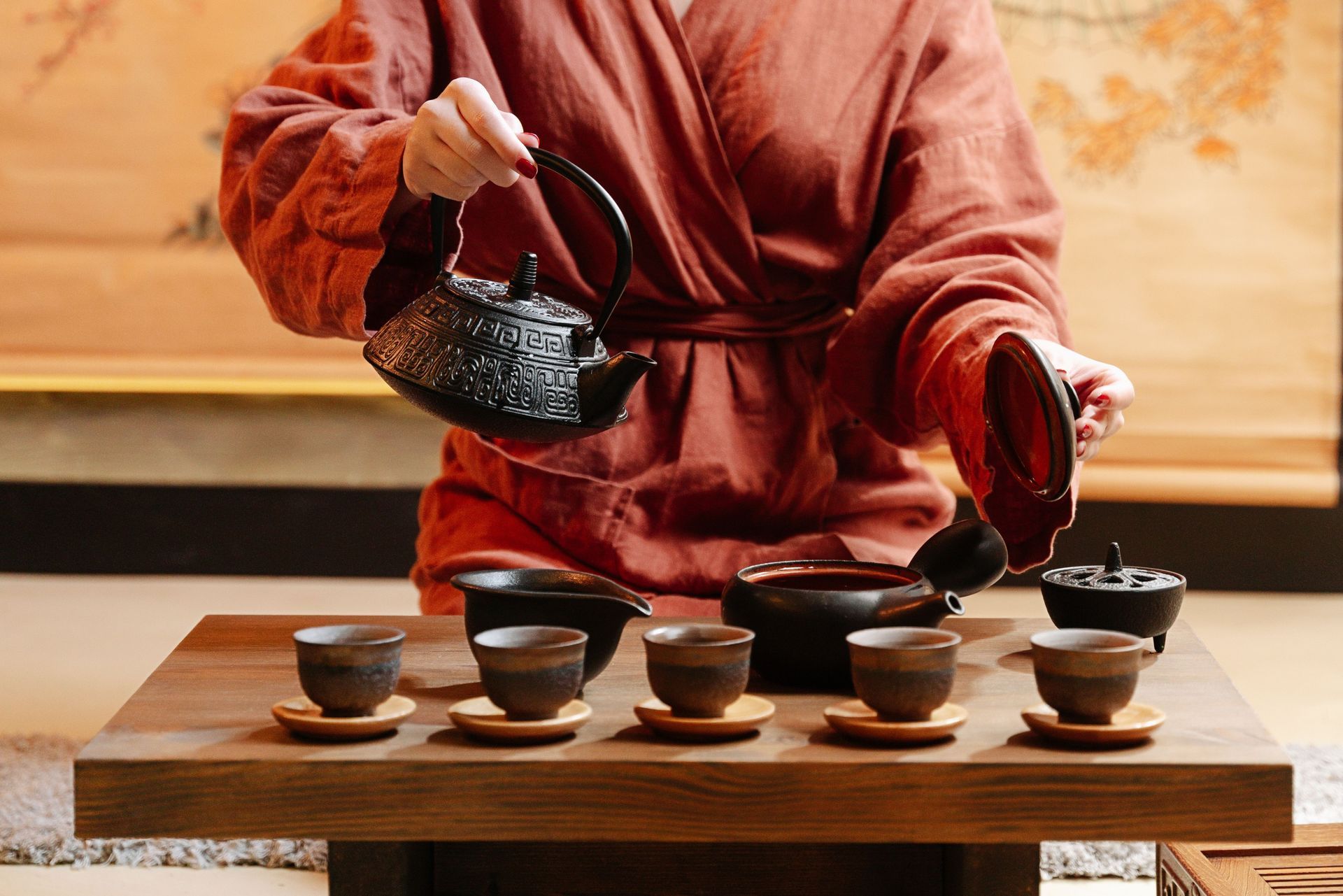 Cérémonie du thé avec une personne versant du thé d'une théière noire dans de petites tasses sur un plateau en bois