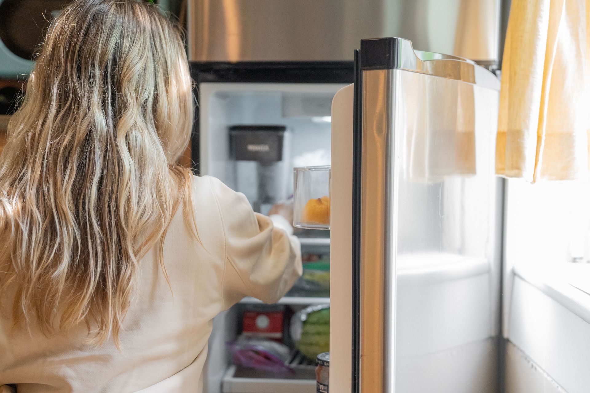 Une femme ouvre un réfrigérateur dans une cuisine lumineuse