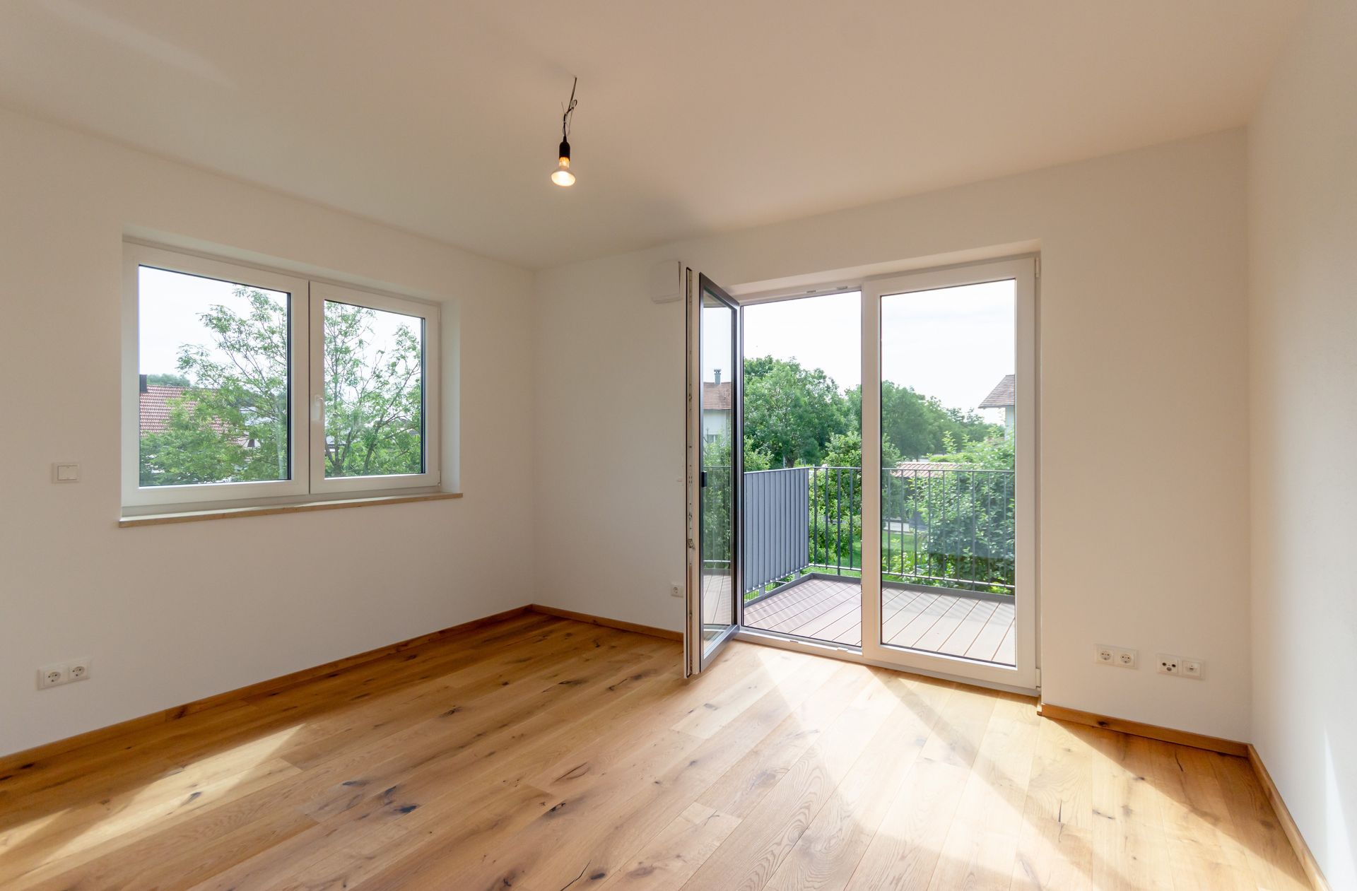 Ein leerer Raum mit Hartholzböden und Glasschiebetüren, die auf einen Balkon führen.