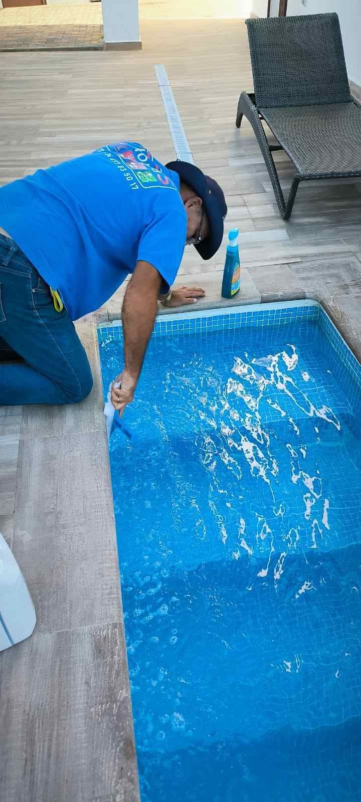 Persona limpiando una piscina azul junto a tumbonas en un patio soleado.