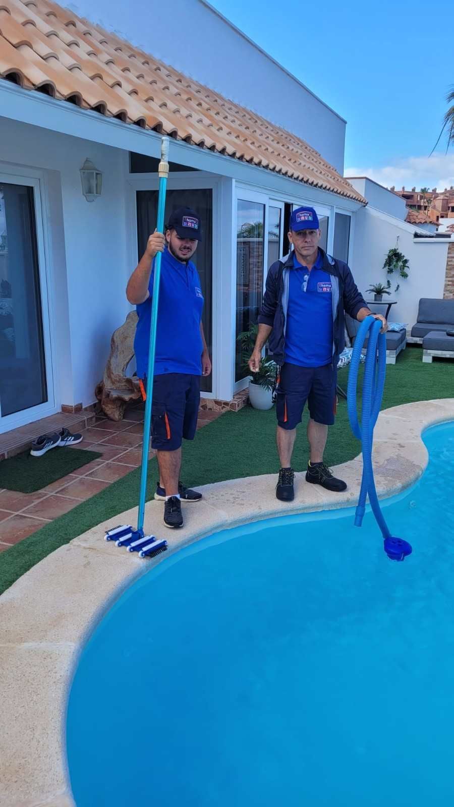 Dos limpiadores de piscinas de pie junto a una piscina en el patio trasero con herramientas de limpieza.