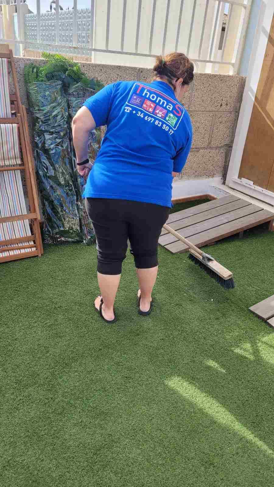 Una persona con una camisa azul se inclina sobre césped artificial junto a una pequeña rampa de madera y una jardinera.