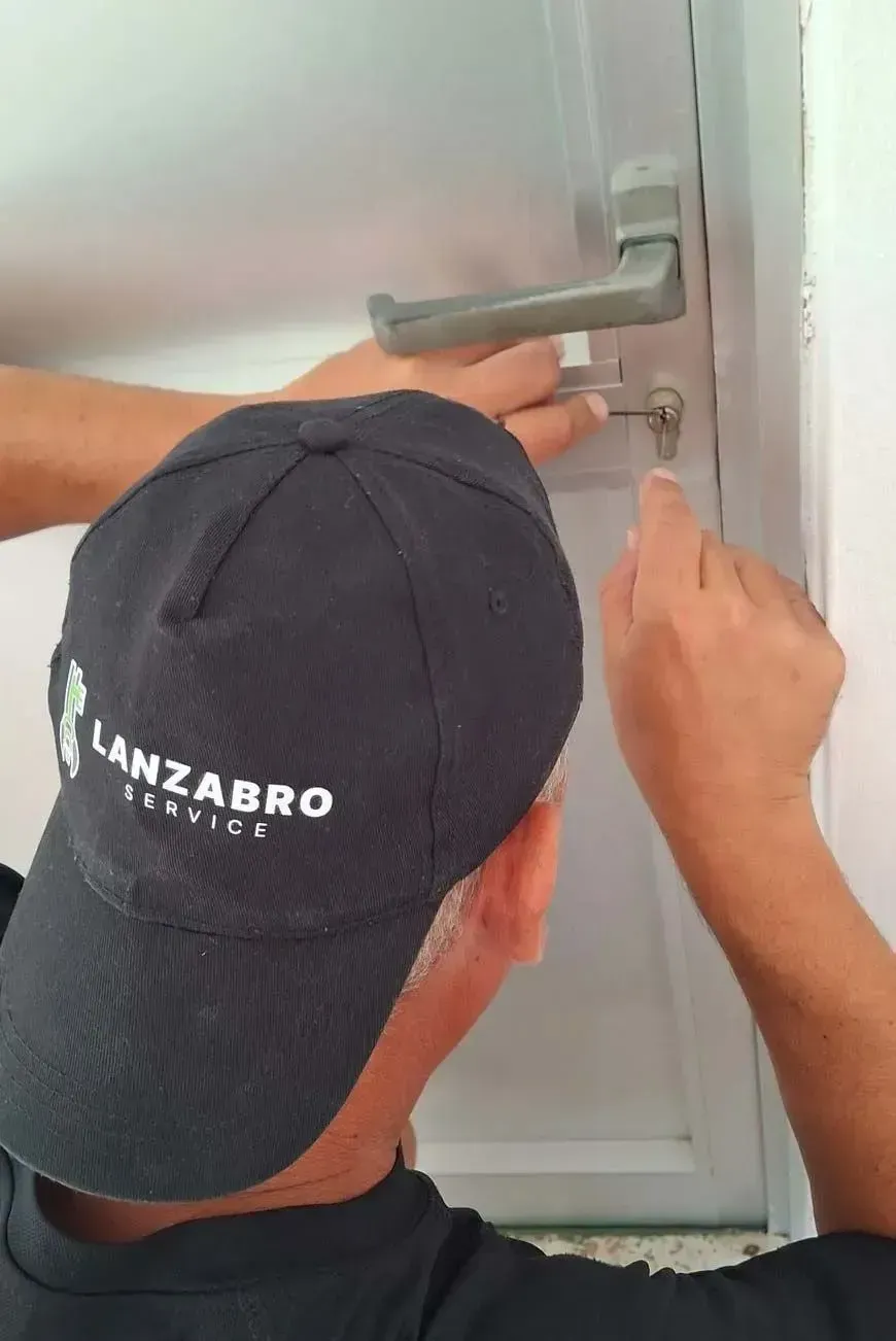 Persona utilizando una llave inglesa para ajustar una lámpara metálica montada en el techo cerca de una puerta.