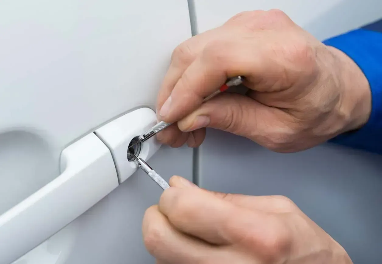 Manos utilizando un destornillador para ajustar la cerradura de la manija de la puerta de un automóvil.