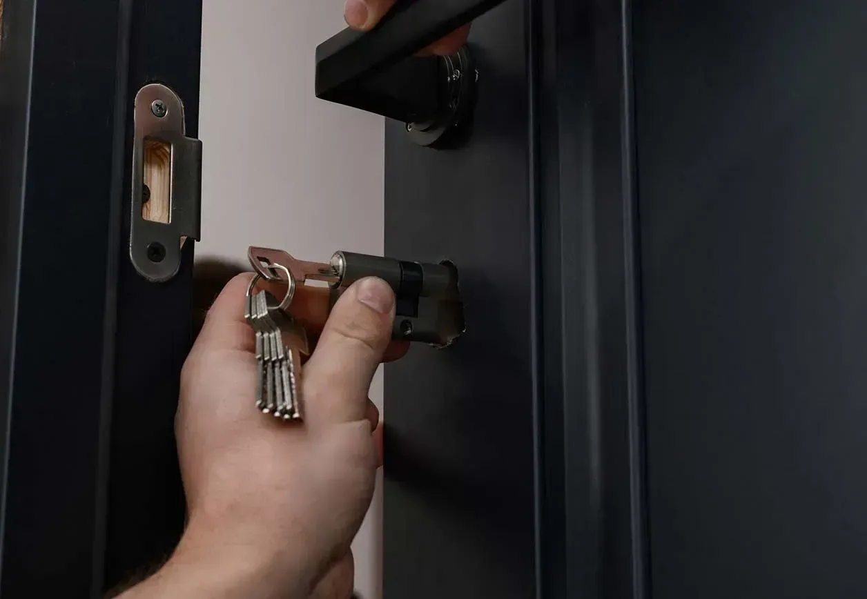 Una mano gira una llave en la cerradura de una puerta, abriendo una puerta de color oscuro.