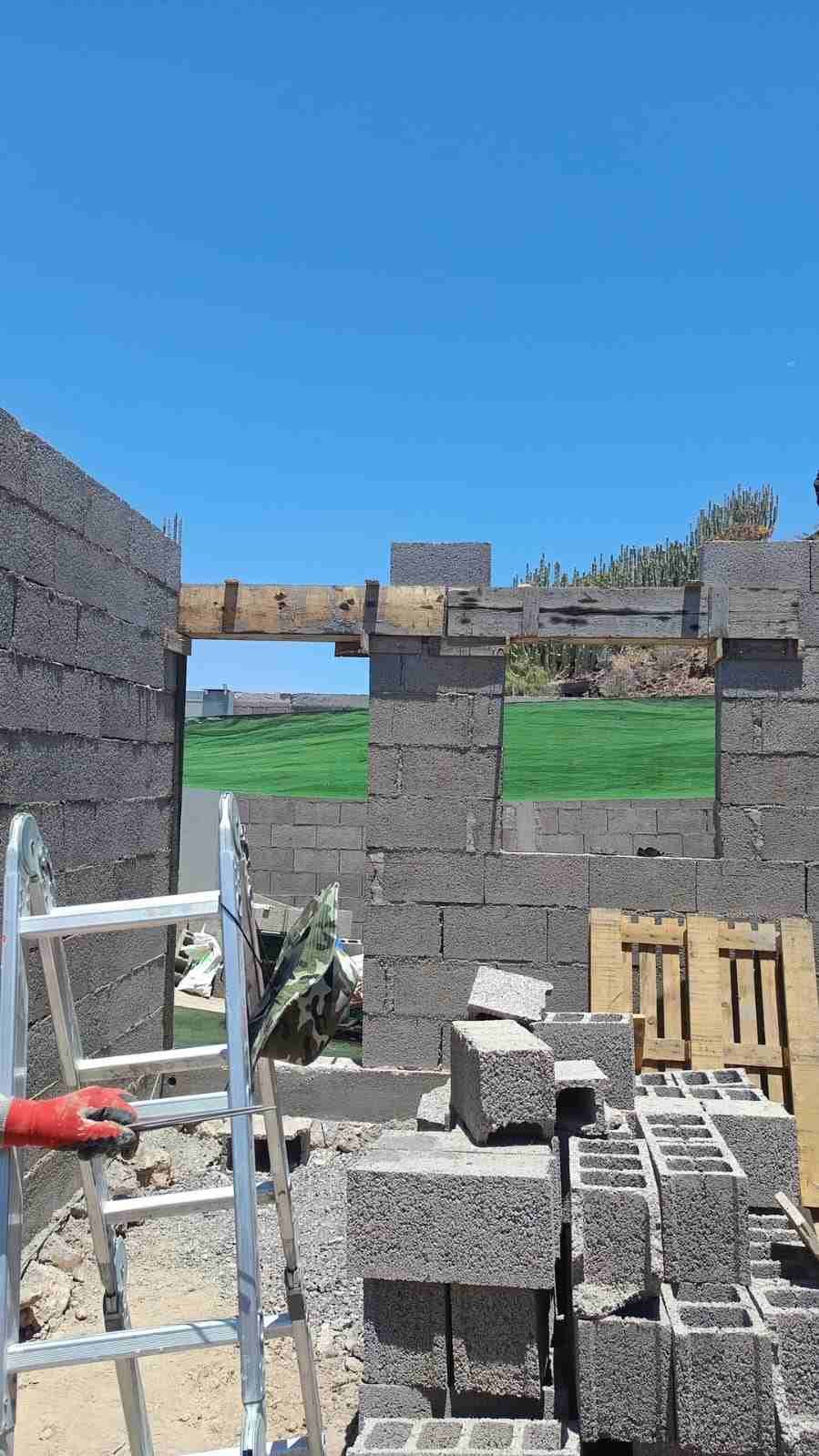 Muro de bloques de hormigón parcialmente construido con escalera, bloques apilados y cielo azul en lo alto.