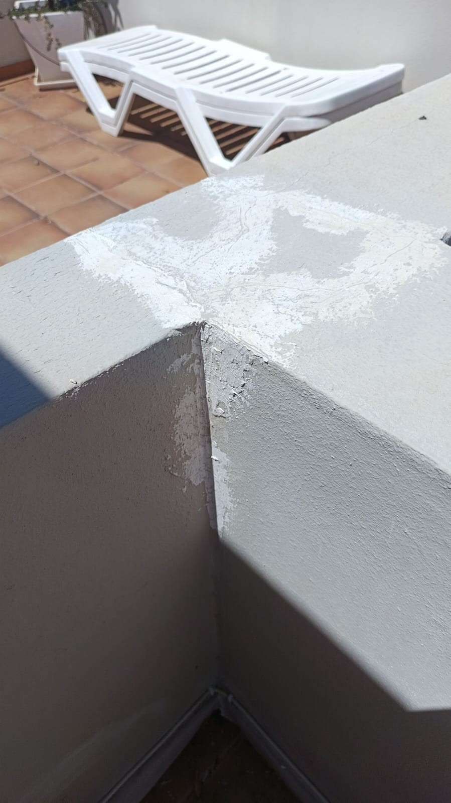 Sillón blanco junto a una pared blanca iluminada por el sol y un rincón de patio con azulejos al aire libre.