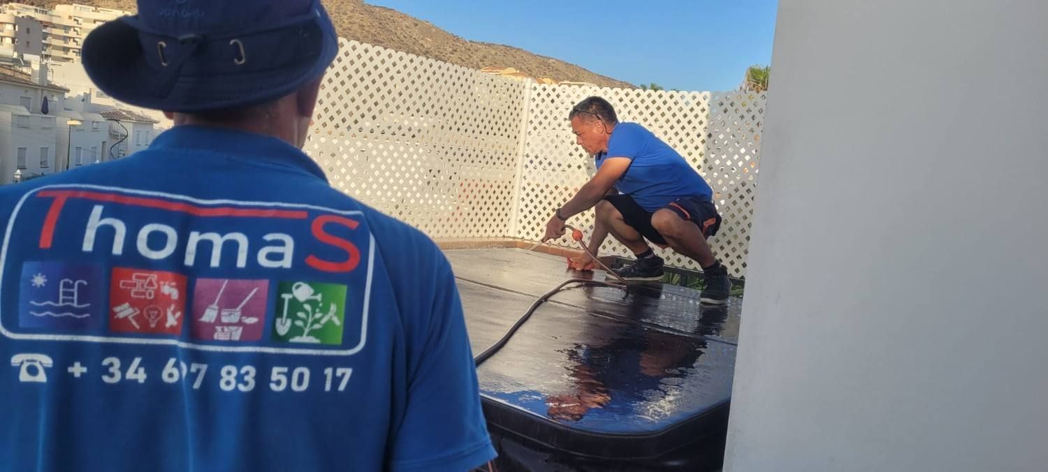 Obreros con camisas azules pintando una pared exterior bajo la luz del sol.