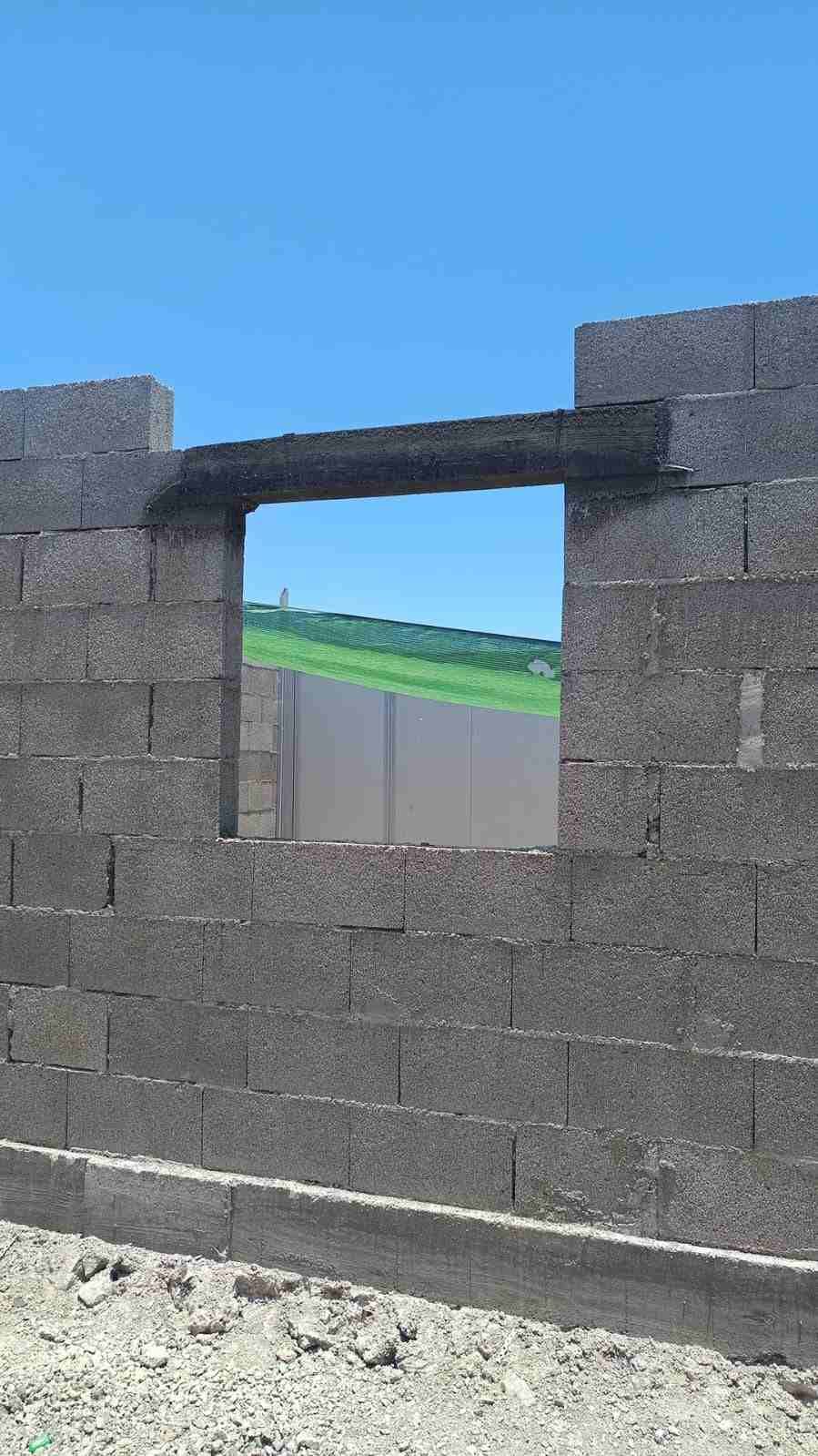 Muro de bloques de piedra con una ventana rectangular que se abre bajo un cielo azul.