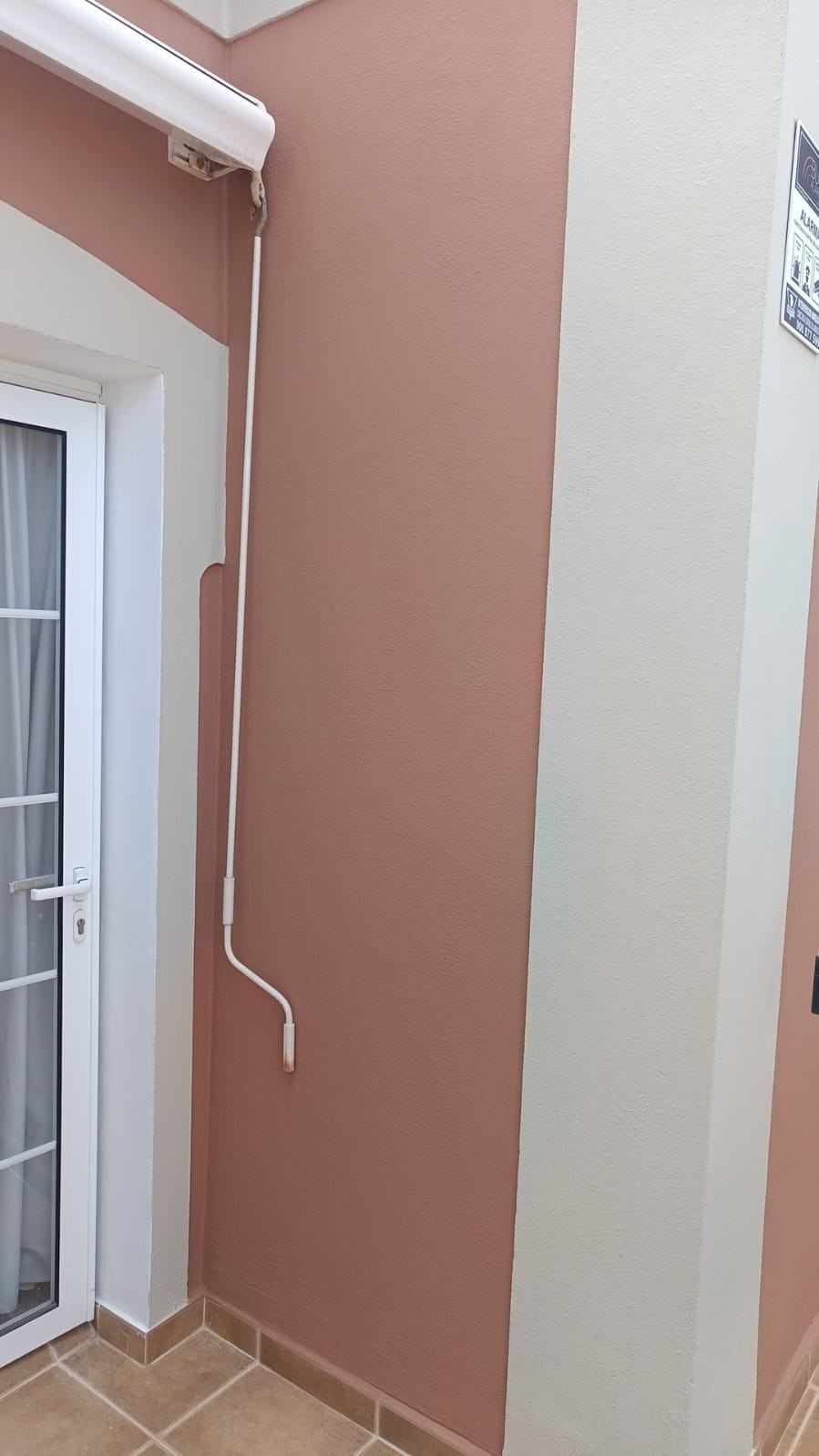 Estrecho pasillo exterior con paredes de color melocotón y beige, suelo de baldosas.